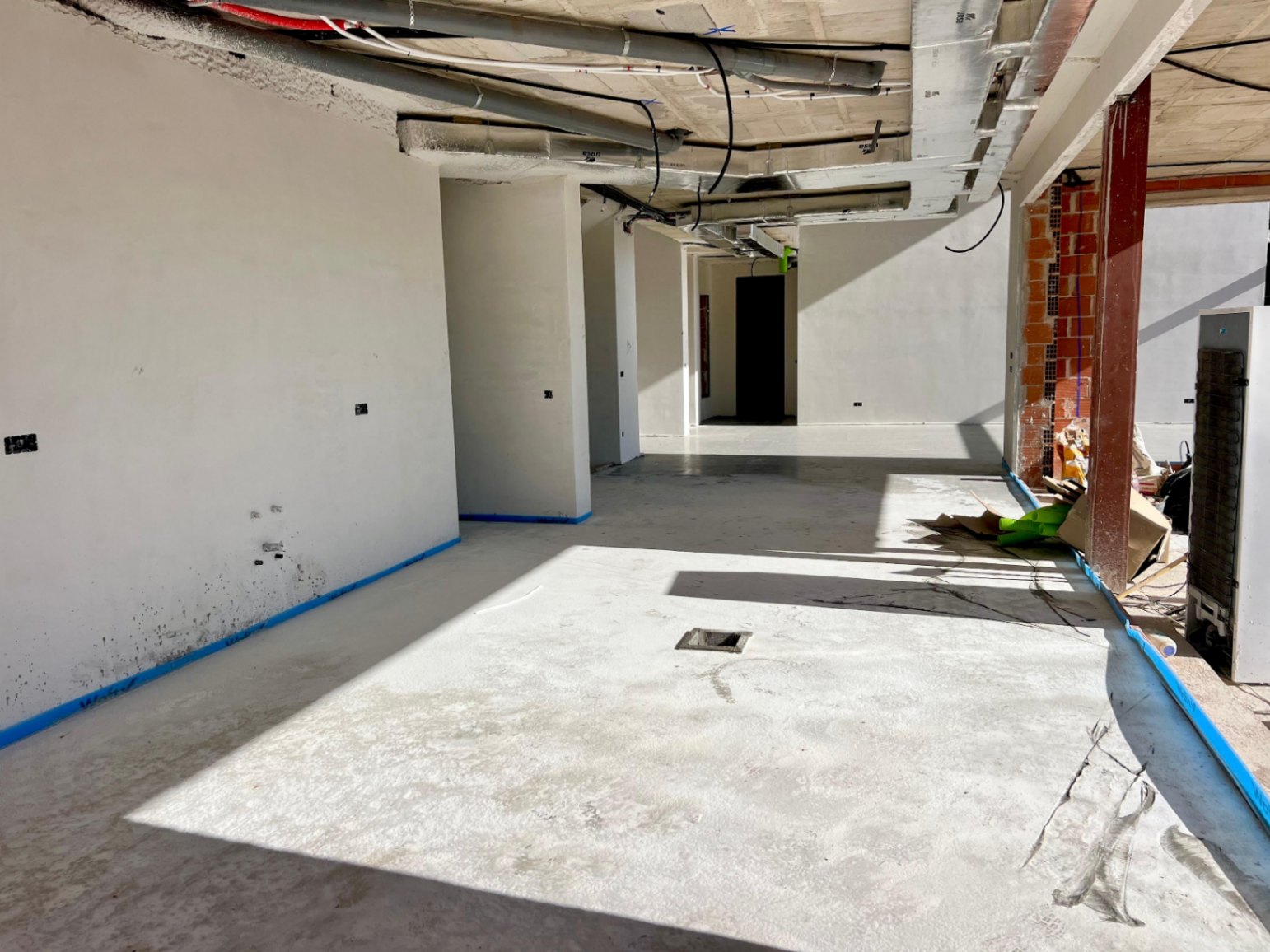 Interior view during construction featuring plastered walls, exposed ceiling utilities, and an open layout designed to capture abundant natural light.