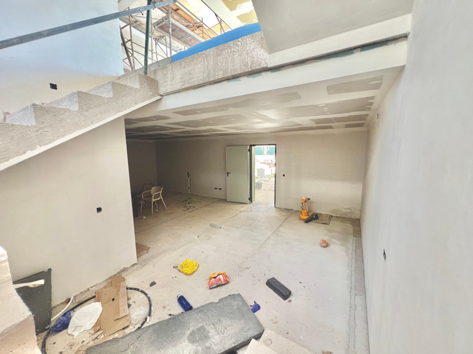 Interior view of the lower level under construction, featuring a structural concrete staircase and versatile open space for a gym or home cinema.