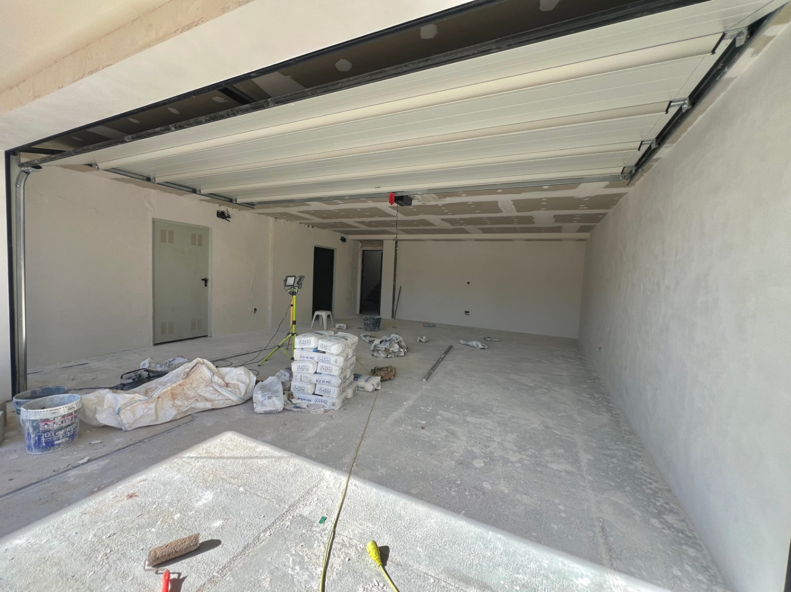 Spacious garage under construction featuring a white sectional door, concrete flooring, and direct access to the villa's interior living areas.