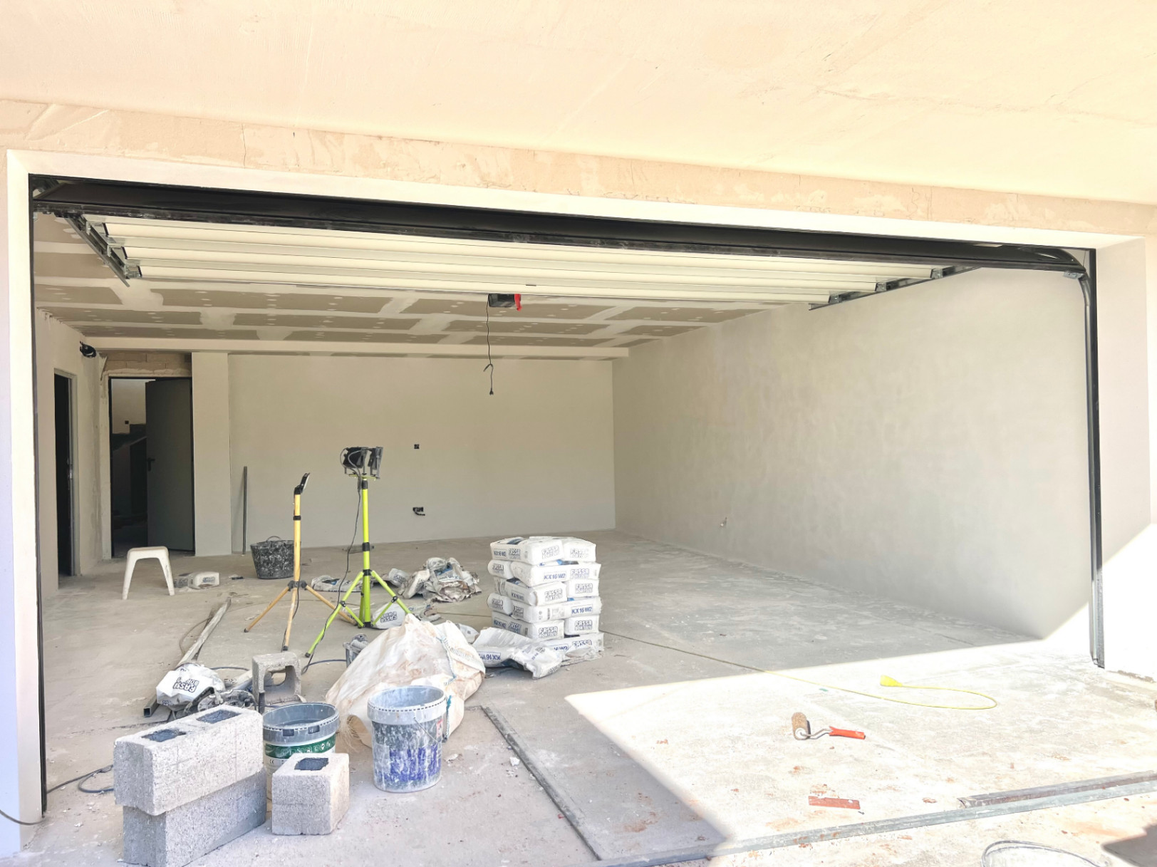 Spacious garage under construction featuring a white sectional door, high ceilings, and an open layout suitable for multiple vehicles or a gym.