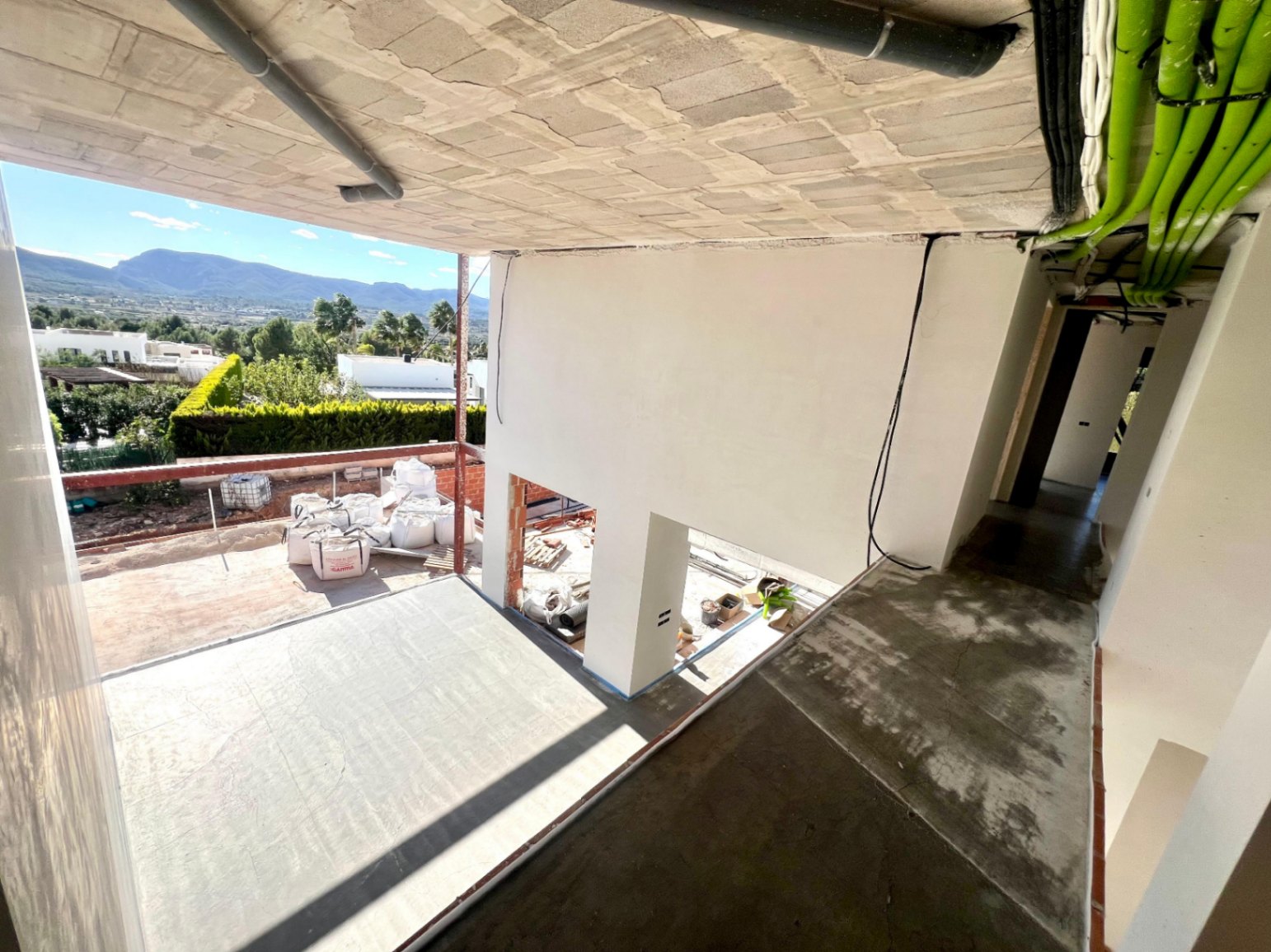 View of the upper floor under construction, highlighting the double-height architectural void and panoramic views of the Montgó mountain and surrounding greenery.