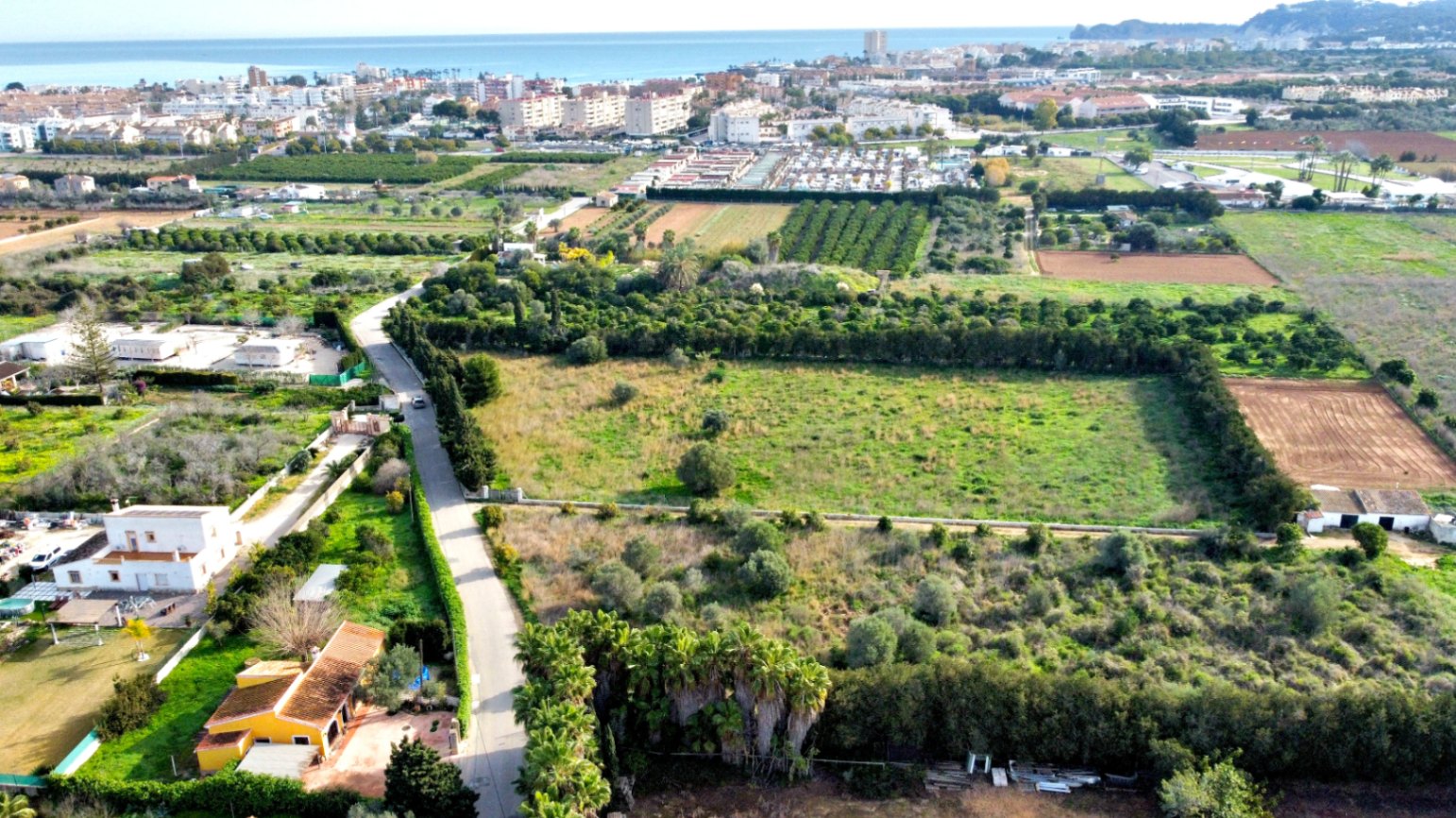 Aerial view of the expansive plot bordered by green hedges, offering clear views of the Mediterranean coastline and nearby town.