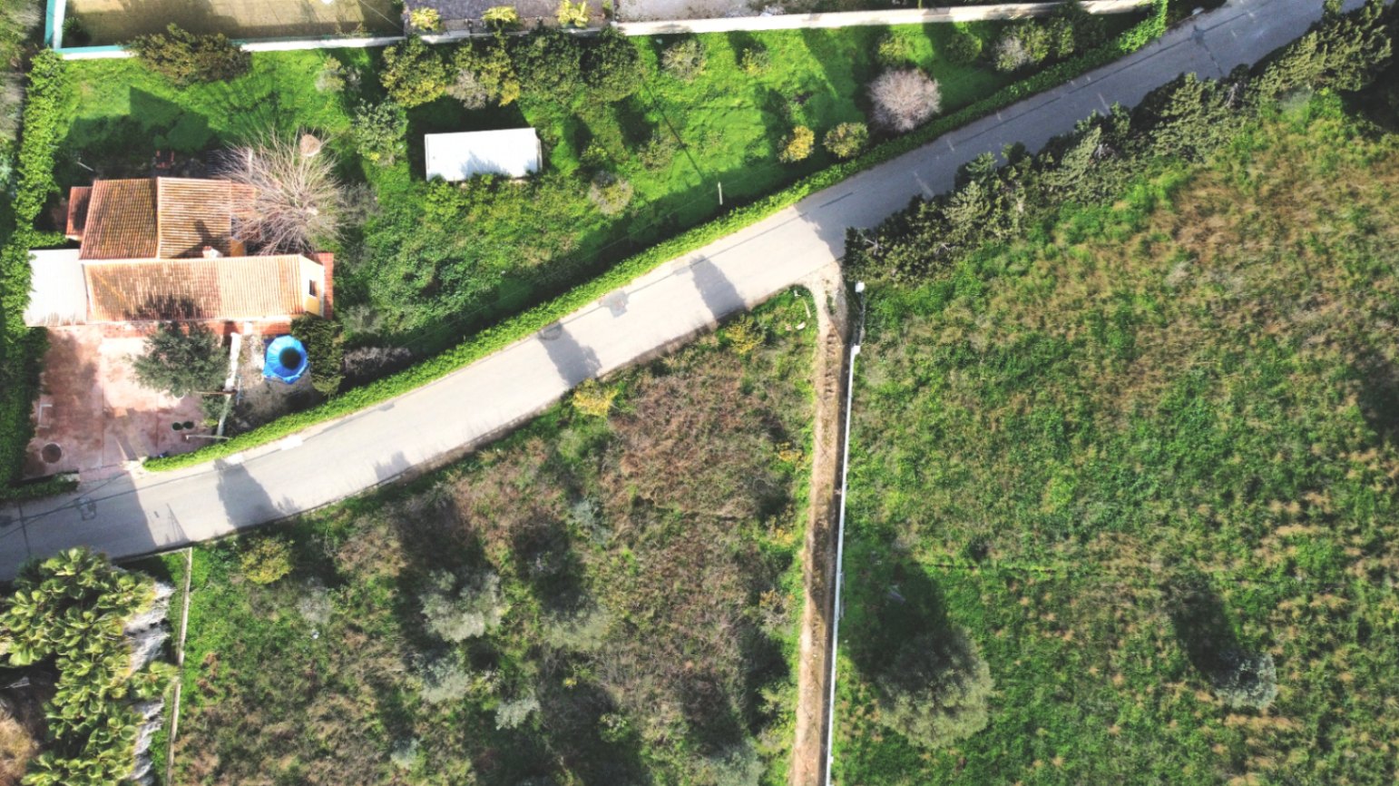 Aerial view of the property featuring the tiled-roof house, the expansive 1,414 sqm plot with Mediterranean greenery, and the paved access road.