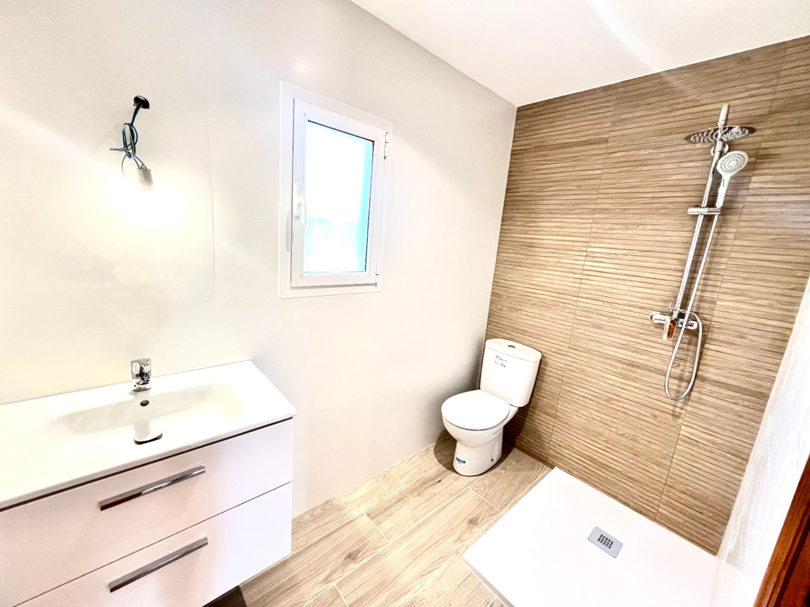 Modern bathroom featuring a walk-in shower with wood-effect tiling, a white vanity unit, and natural light from a side window.