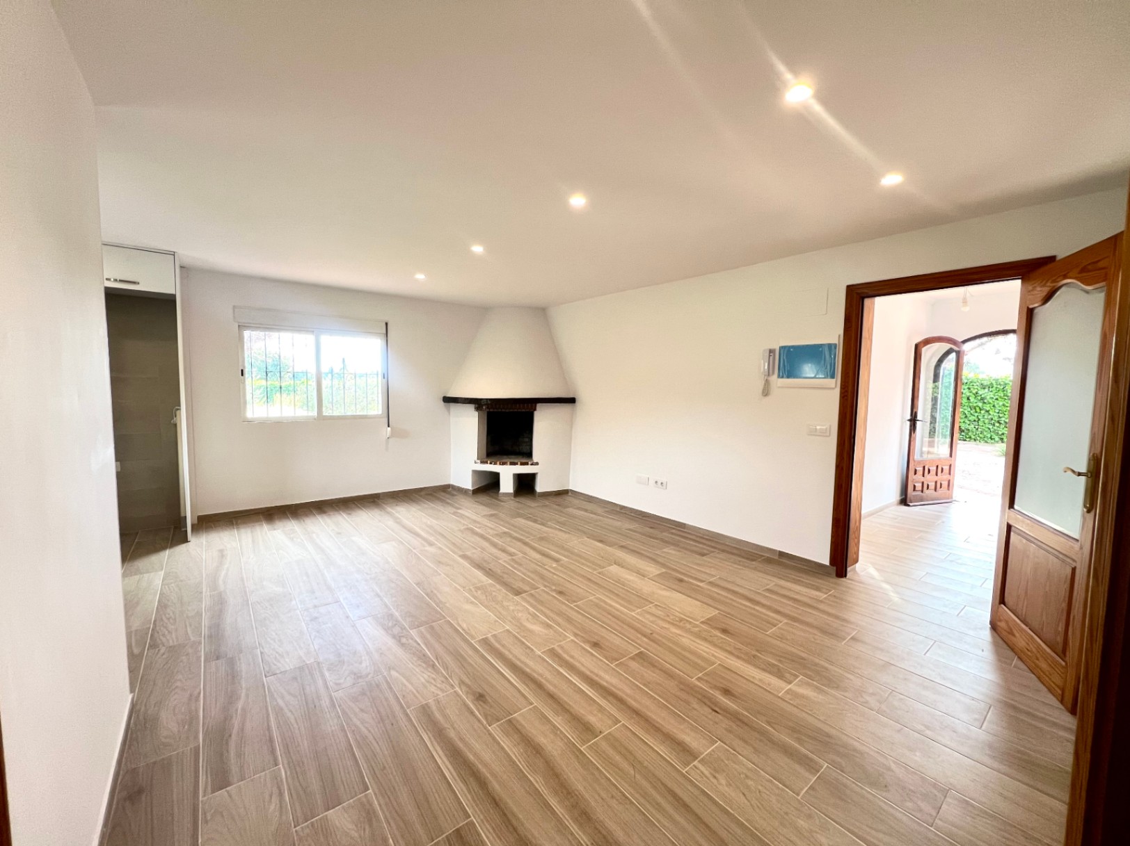 Spacious living area featuring a corner fireplace, recessed ceiling lighting, and wood-effect ceramic flooring. Large wooden doorways lead to the bright entrance hall.