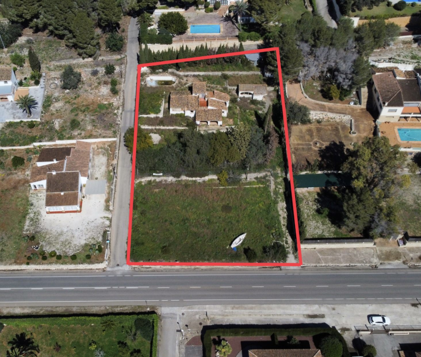 Aerial view of the 2,895m2 plot in Montgó, Jávea, featuring the main house, outbuildings, and a large flat garden area with direct road access, outlined in red.