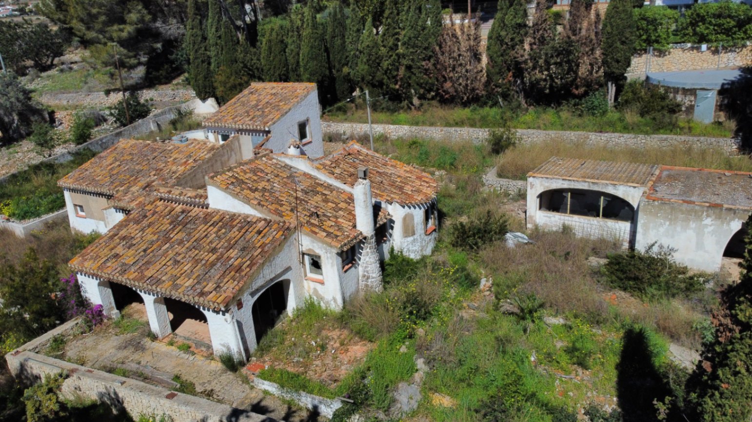 Aerial view of the Mediterranean villa featuring traditional terracotta roofs, arched porches, and a stone chimney, set within an expansive, natural plot.