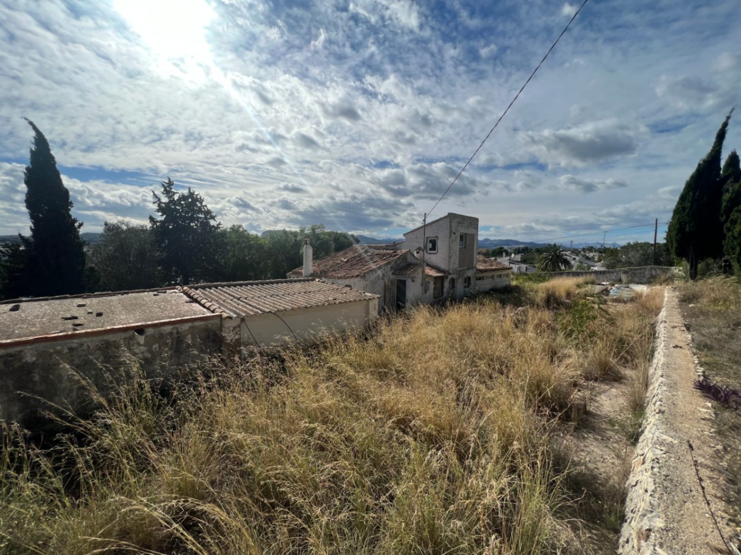Exterior perspective of the original structure and tiled outbuildings, highlighting the expansive plot and the comprehensive renovation project available in the Montgó area.