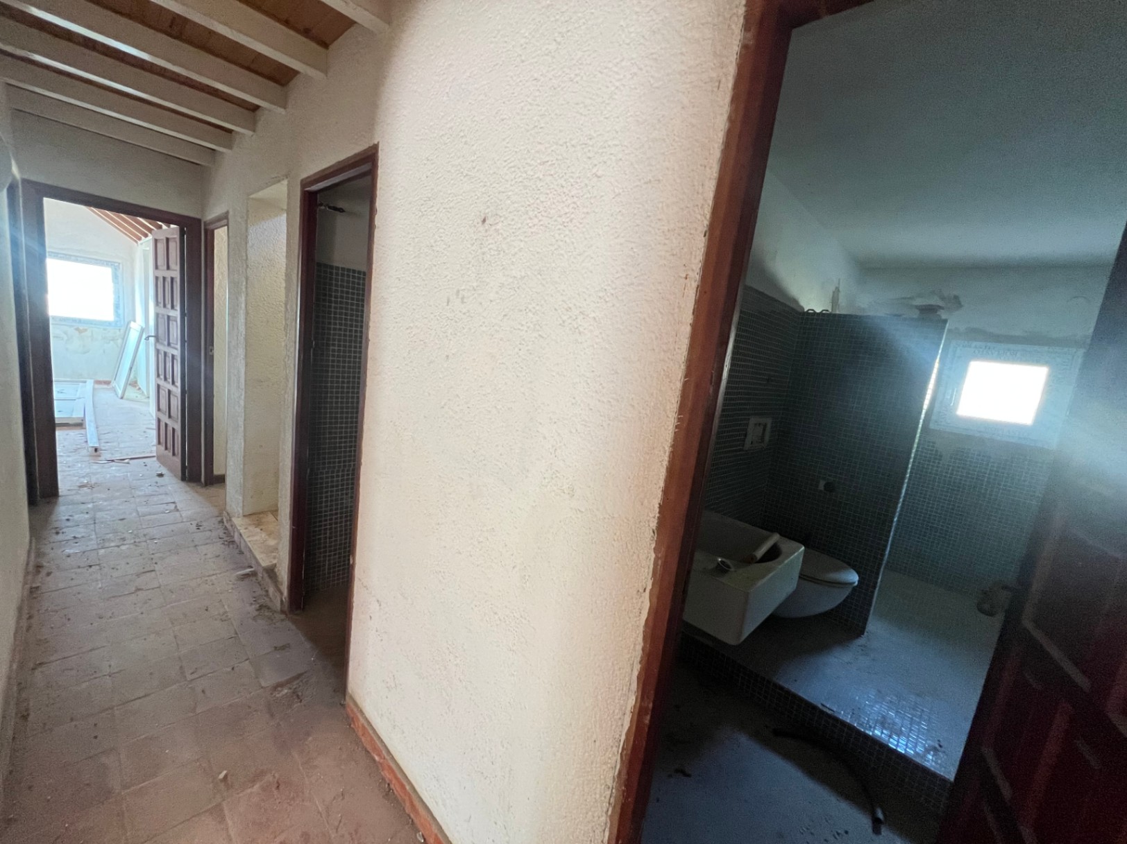 Interior hallway featuring exposed wooden ceiling beams and access to a bathroom with blue mosaic tiles. The space highlights the property's renovation potential.