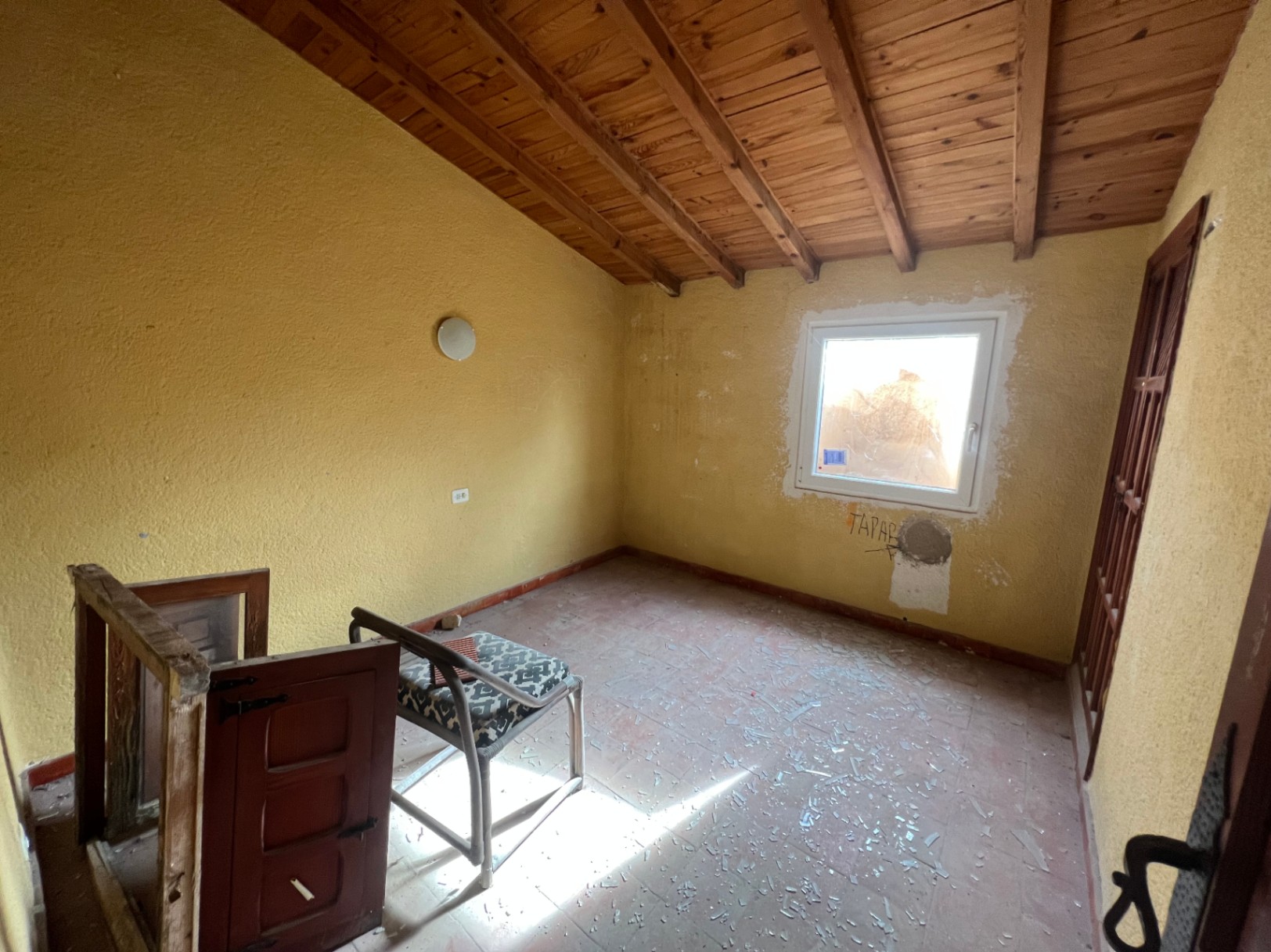Interior room featuring a sloped wooden beam ceiling, terracotta tile flooring, and yellow walls. This space requires a full renovation and offers natural light.