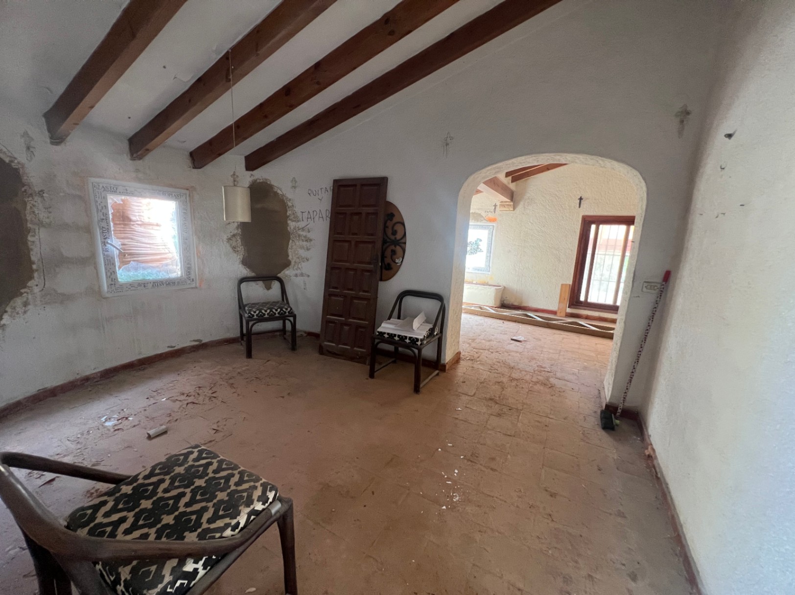 Interior room undergoing renovation featuring exposed wooden ceiling beams, terracotta tile flooring, and a traditional arched doorway.