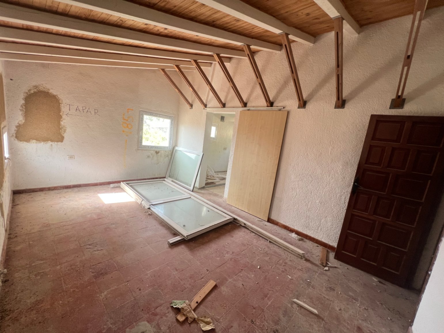 Interior room undergoing renovation featuring exposed wooden ceiling beams, traditional terracotta tile flooring, and new window frames ready for installation.