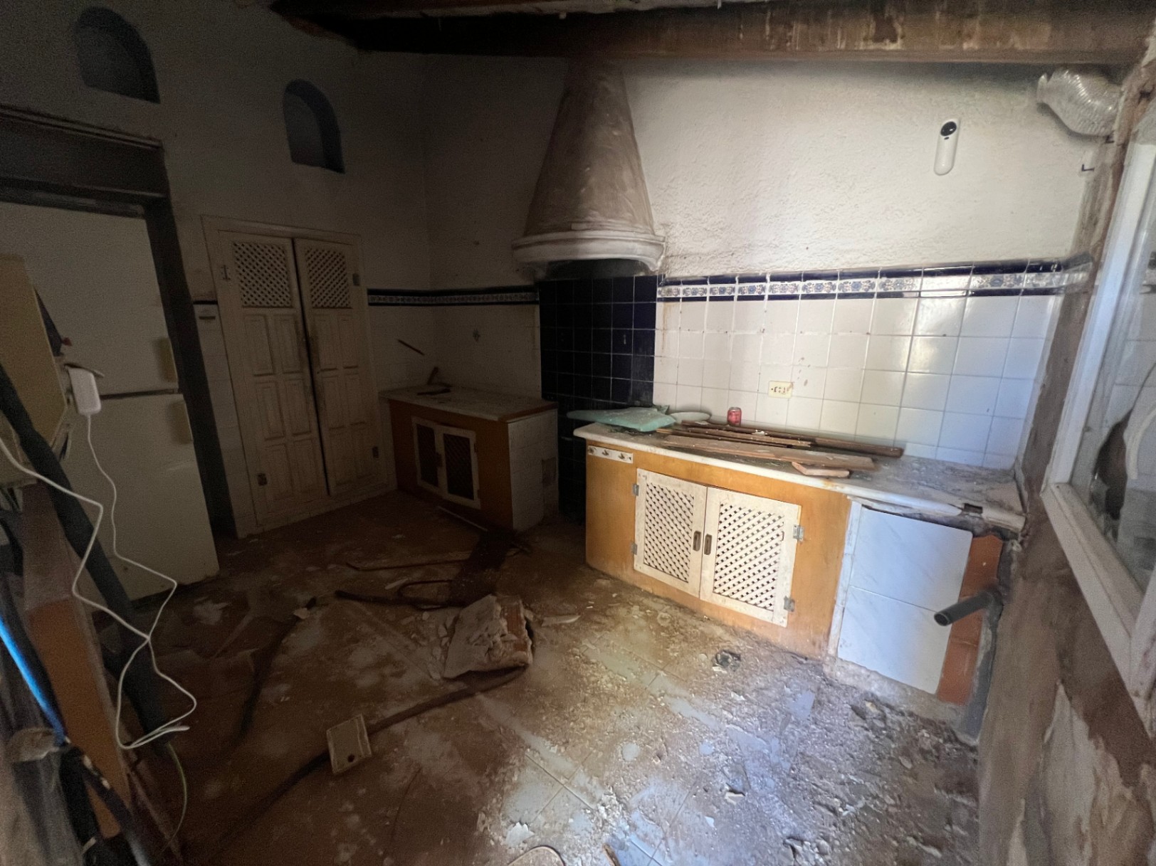 Rustic kitchen requiring renovation, featuring a conical plaster hood, traditional blue and white tiling, wooden latticed cabinetry, and decorative wall niches.