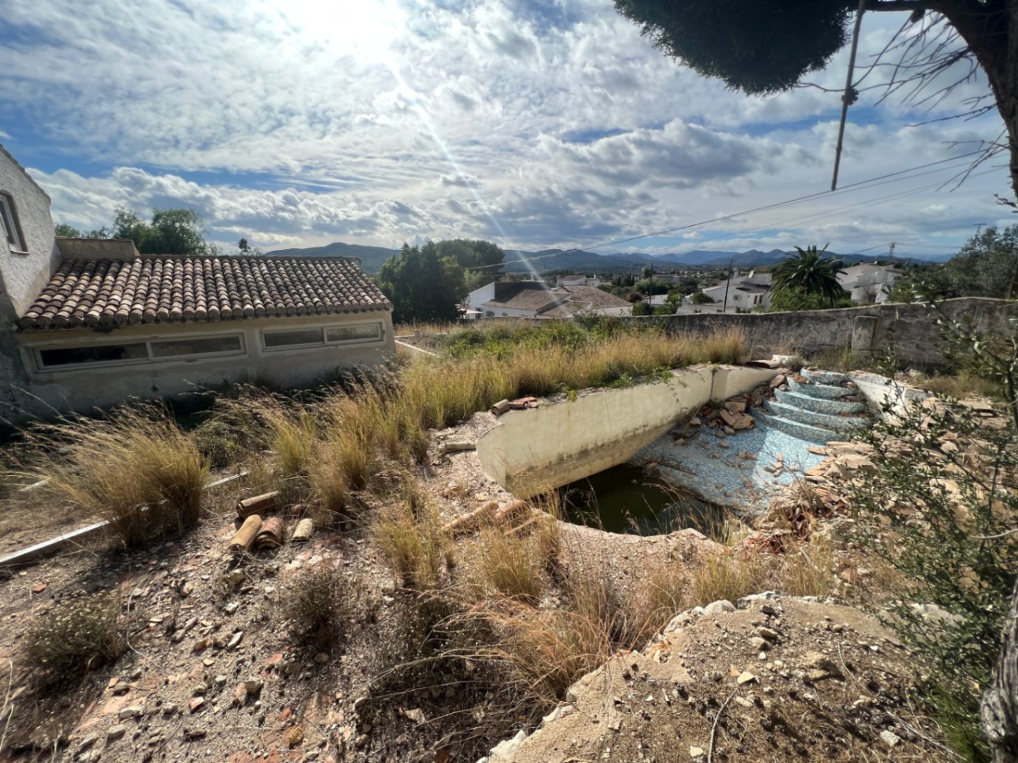 Swimming pool in need of renovation set within a natural landscape, offering open mountain views and an adjacent traditional tiled outbuilding.