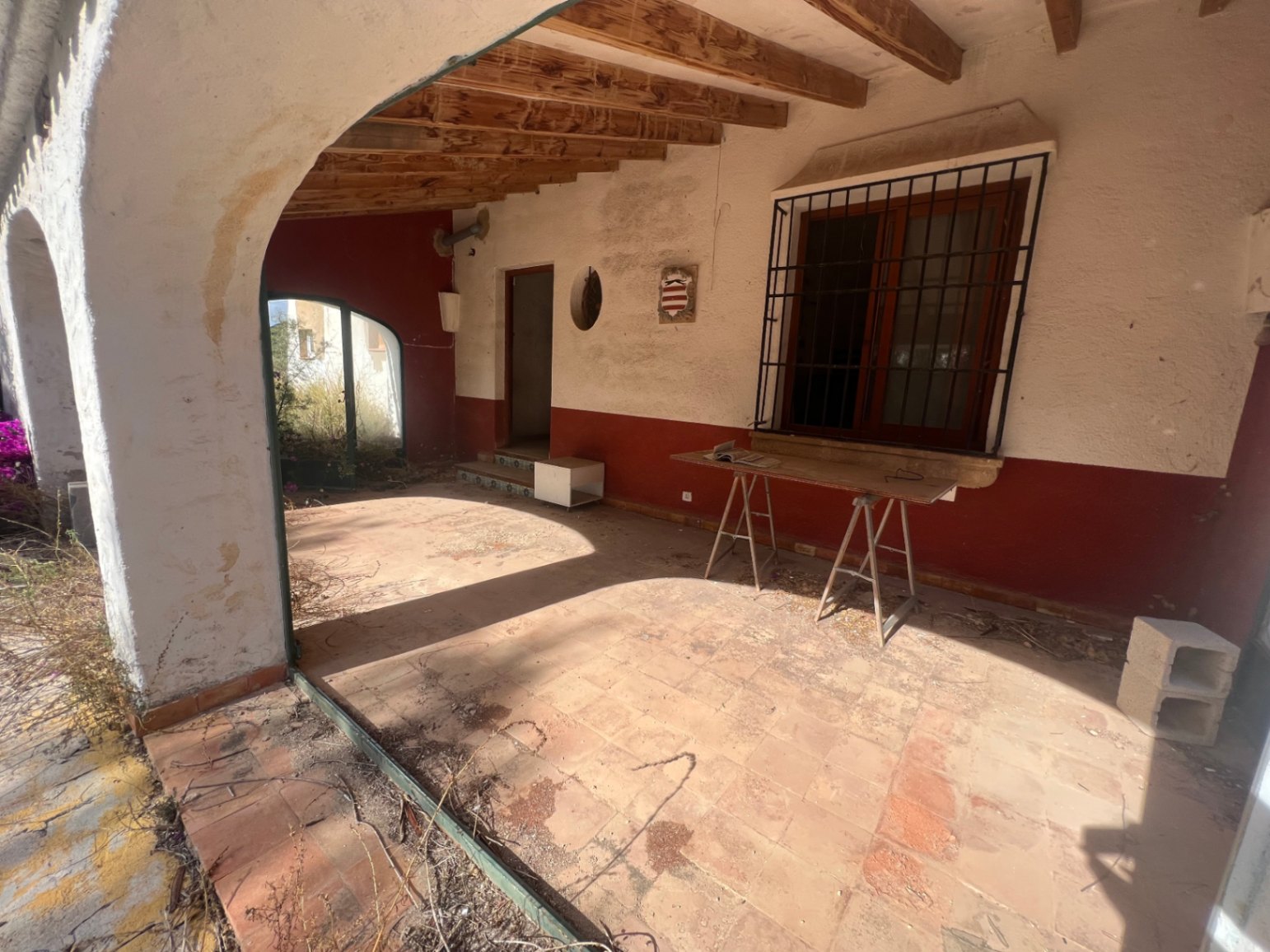 Traditional covered terrace featuring exposed wooden beams, terracotta tile flooring, and Mediterranean arches overlooking the garden area.