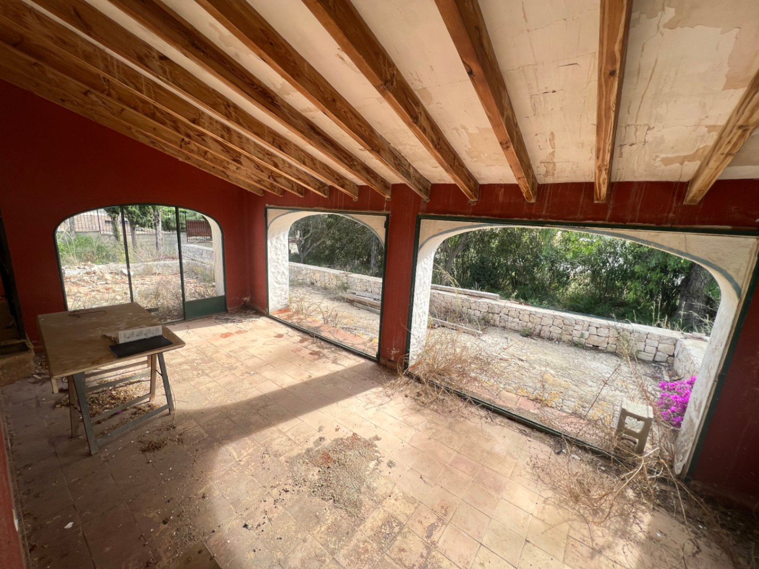 Traditional naya featuring exposed wooden ceiling beams, terracotta flooring, and large arched windows overlooking the garden and stone perimeter walls.