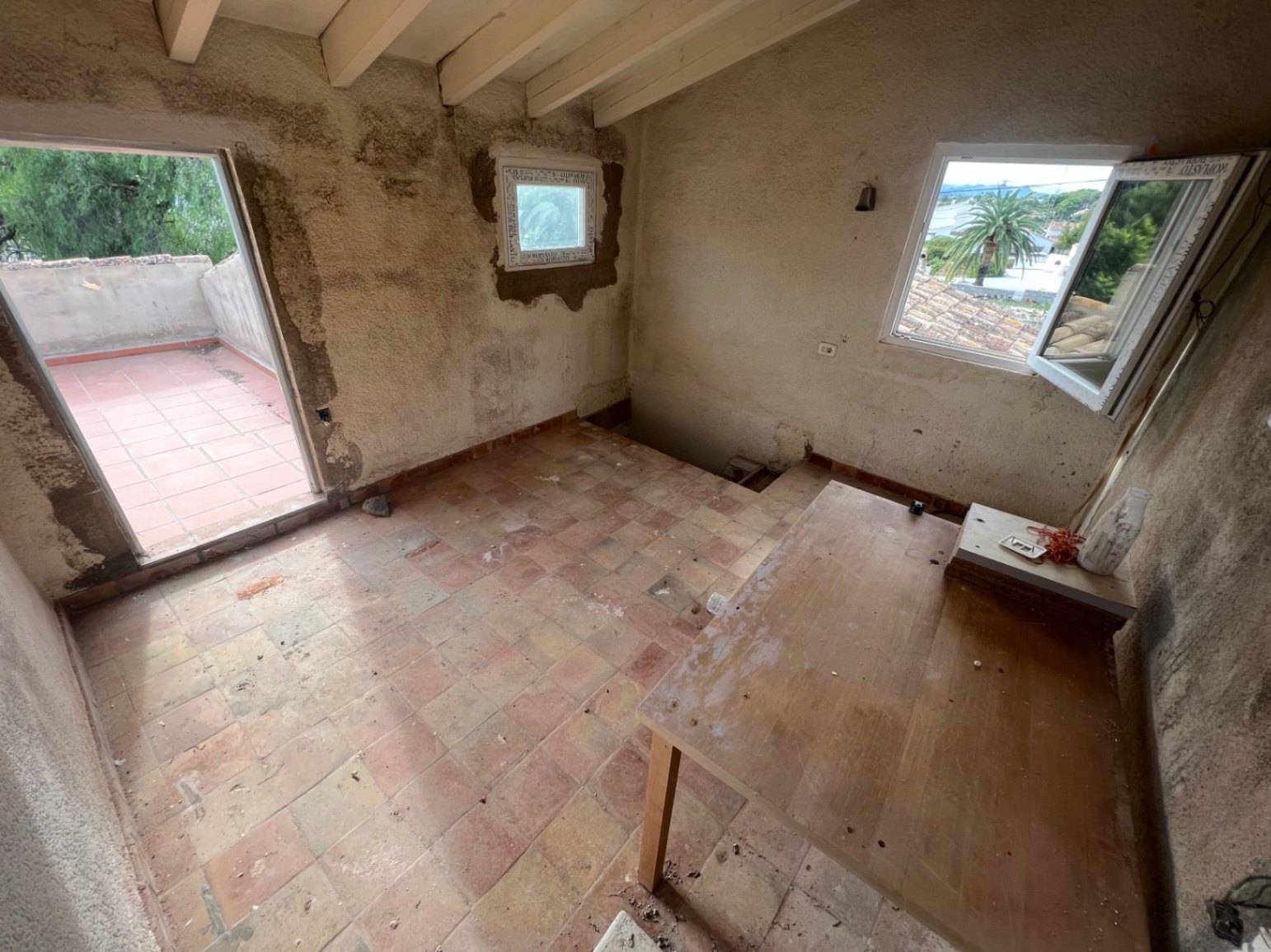 Upper floor room requiring renovation, featuring exposed ceiling beams, terracotta flooring, and direct access to a private sun terrace.