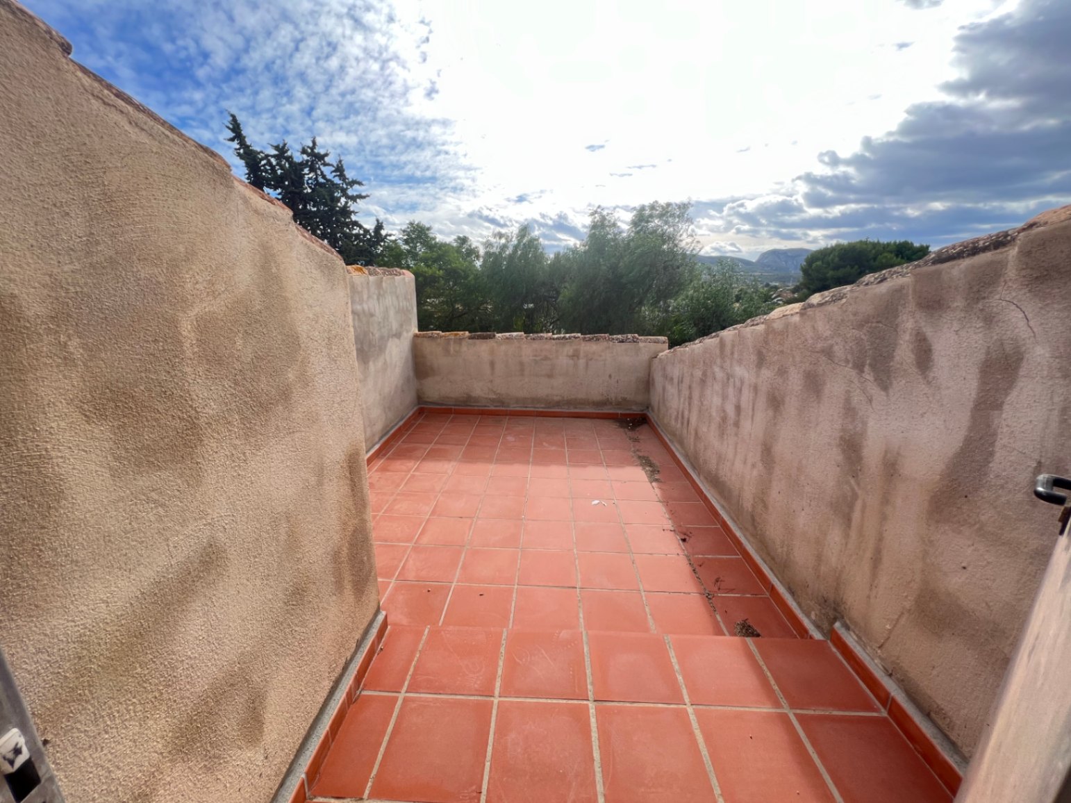 Upper-level terrace featuring traditional terracotta tiling and high privacy walls, overlooking the lush Mediterranean greenery and distant mountain peaks.