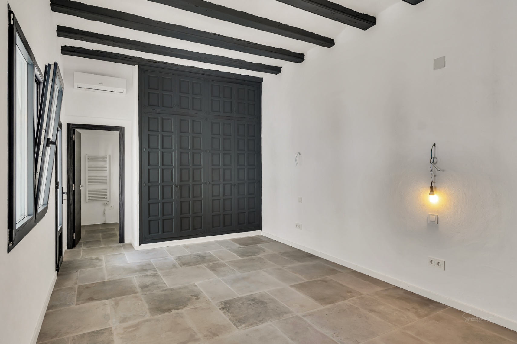 Bedroom featuring dark exposed wooden ceiling beams, natural stone flooring, and a large charcoal grey built-in wardrobe with traditional paneling.