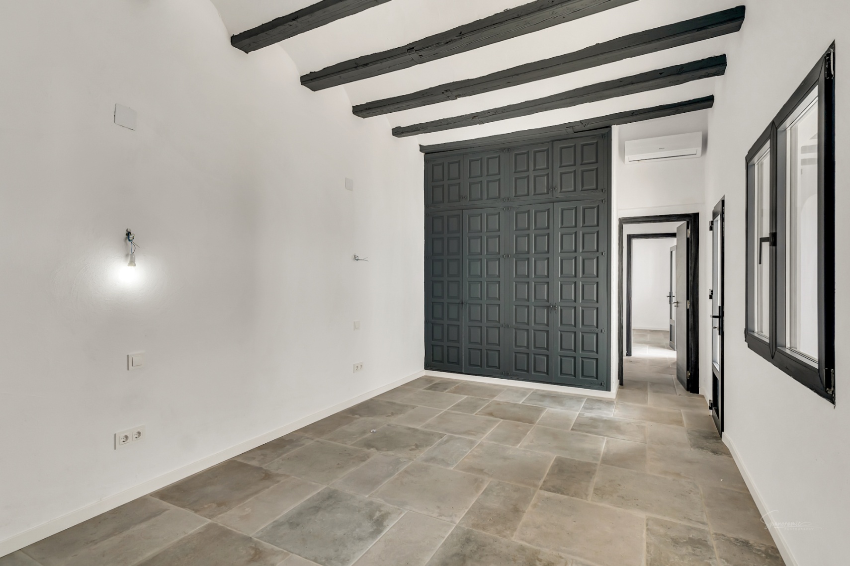 Bedroom featuring dark wooden ceiling beams, natural stone flooring, and a large built-in wardrobe with charcoal grey paneled doors.
