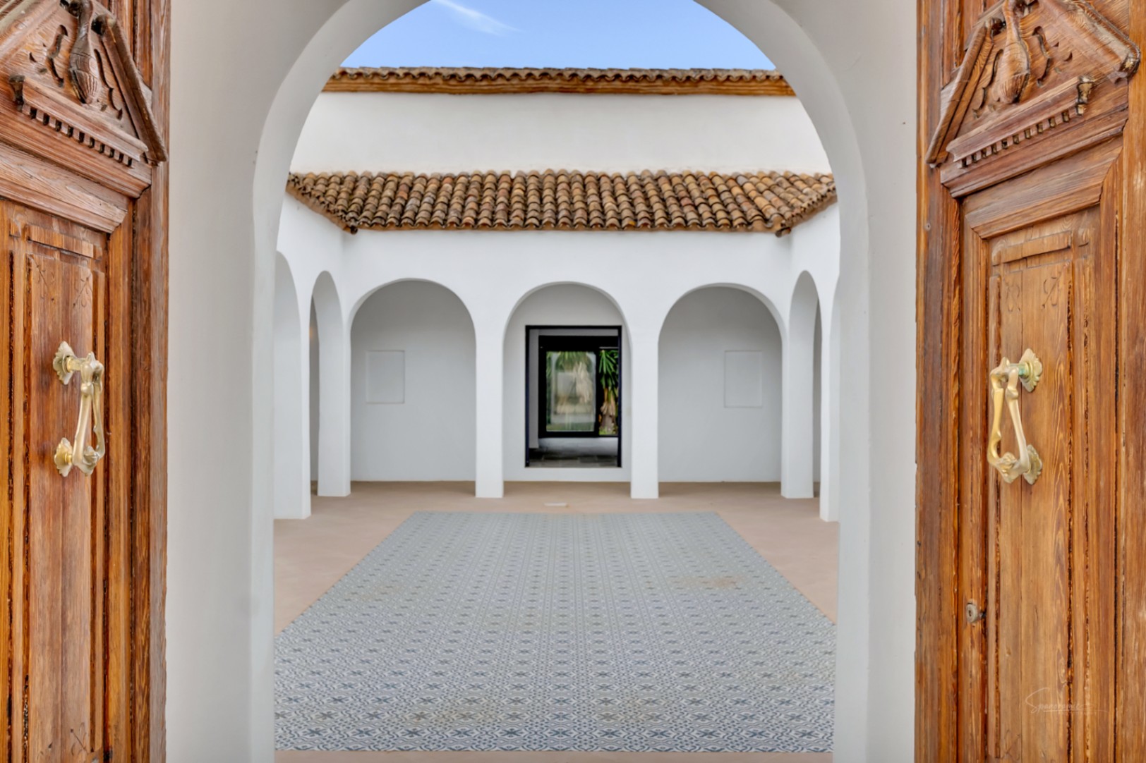 Central interior courtyard featuring elegant white arches, decorative patterned floor tiles, and traditional carved wooden entrance doors.