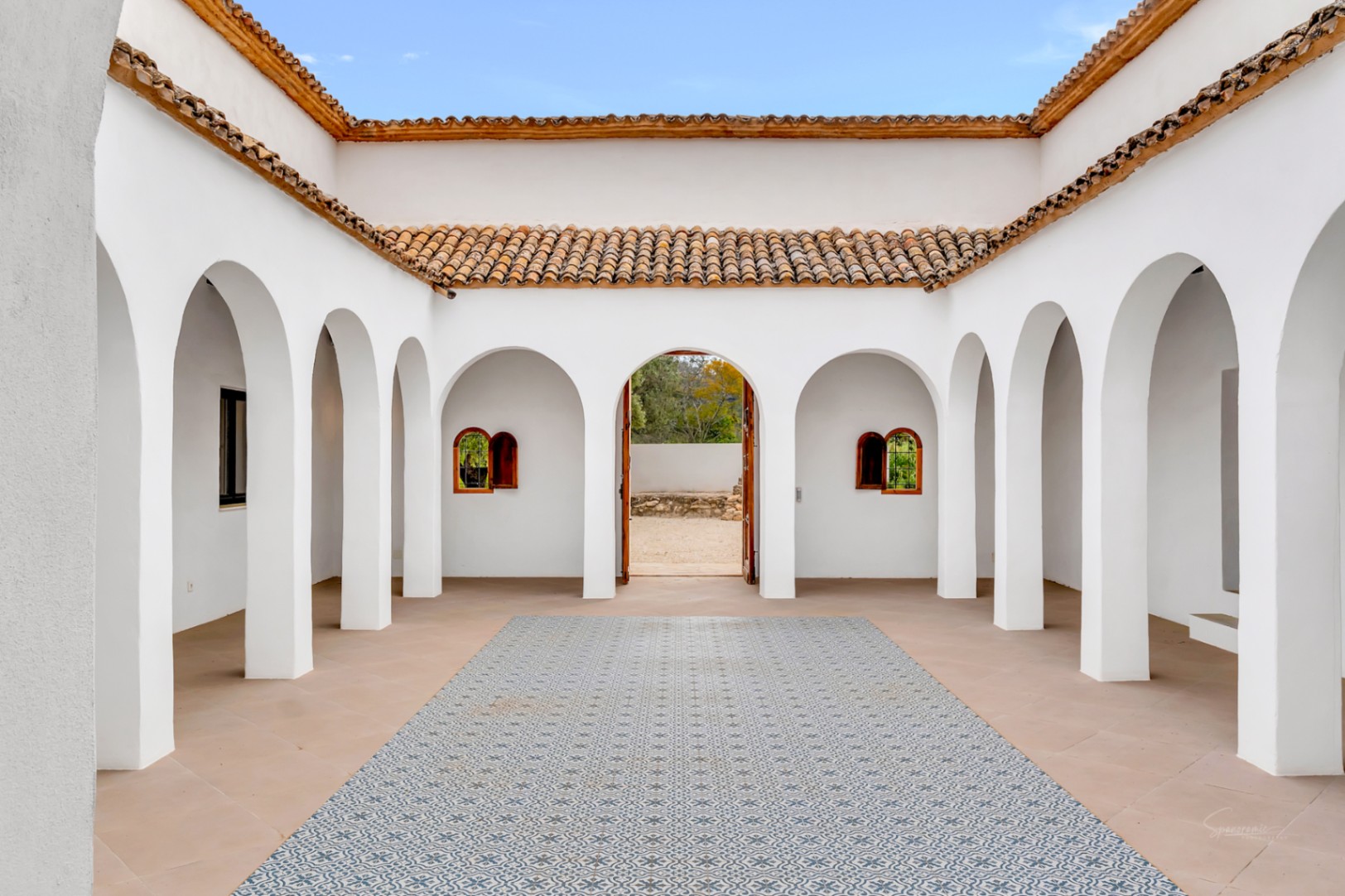 Central interior courtyard featuring white arched colonnades, patterned decorative tiling, and traditional terracotta rooflines under an open sky.
