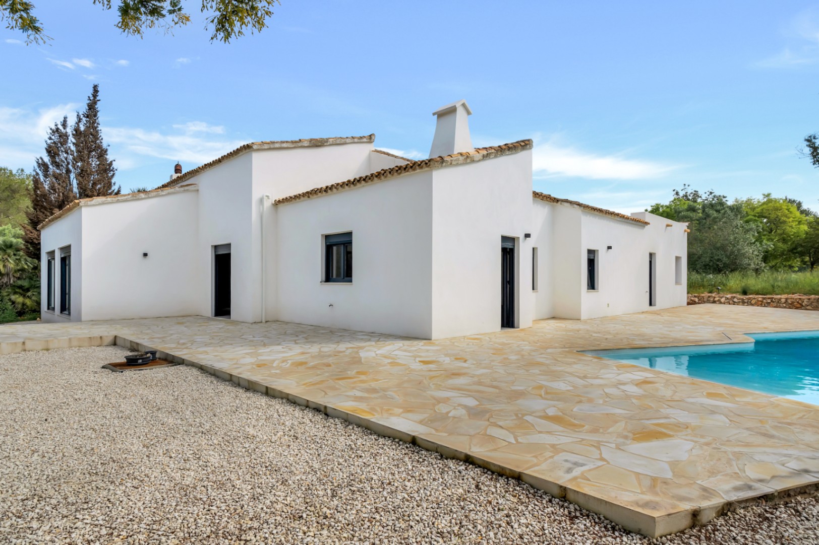Exterior of the single-story villa featuring white stucco walls, a large flagstone terrace, and a swimming pool area.