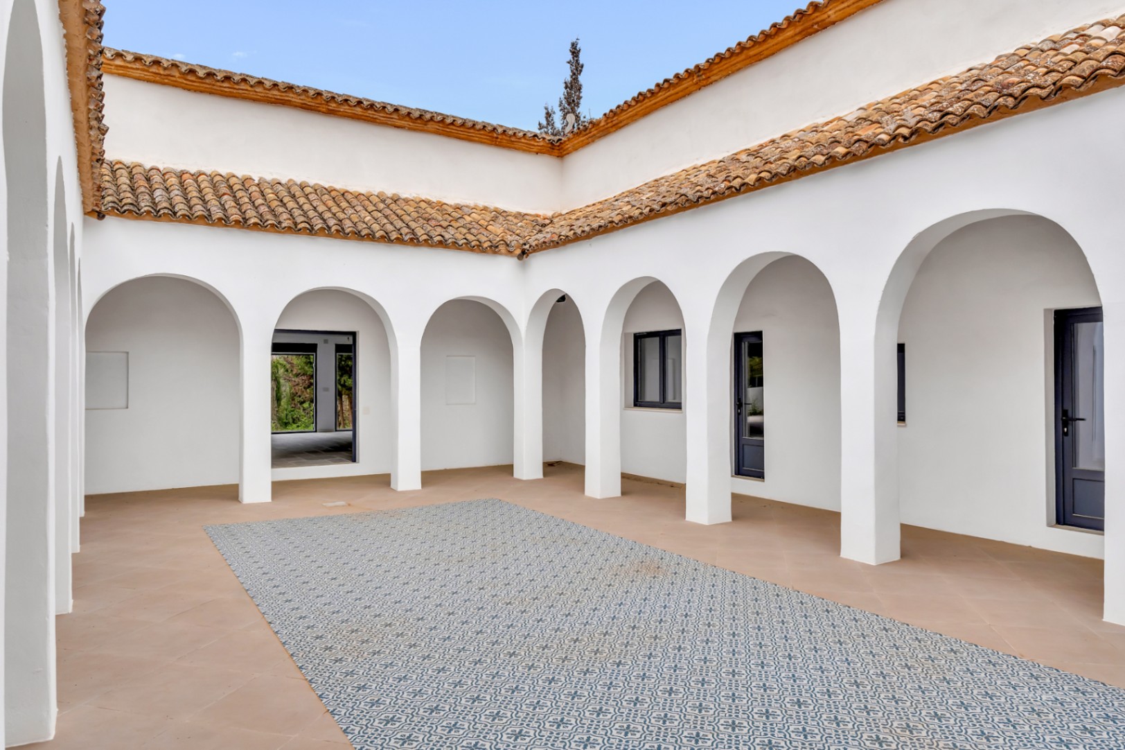 Mediterranean-style interior courtyard featuring white arches, terracotta flooring with a central patterned tile mosaic, and traditional clay roof tiles.