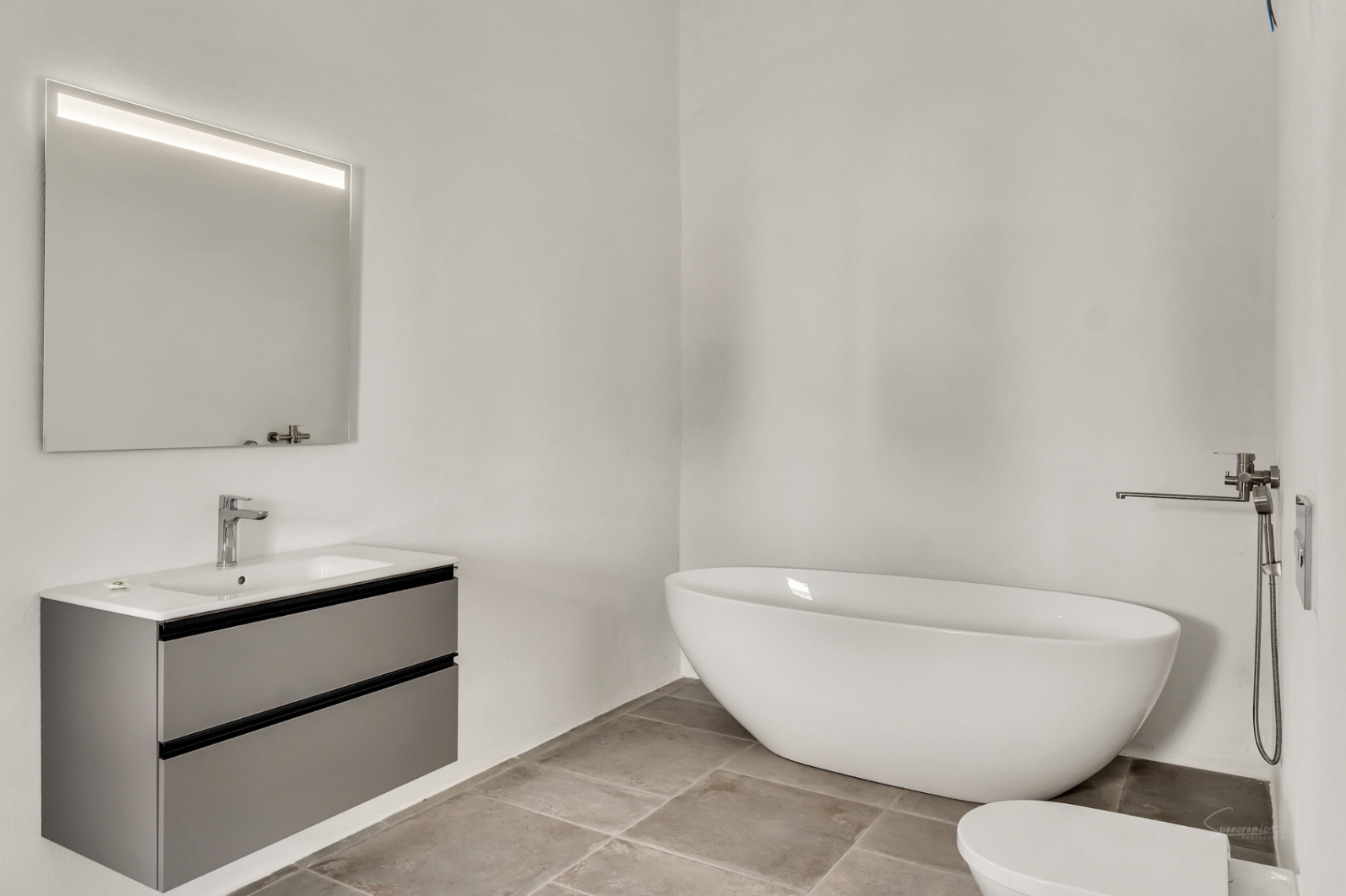 Modern bathroom featuring a freestanding oval bathtub, a floating grey vanity with integrated sink, and natural stone flooring against minimalist white walls.