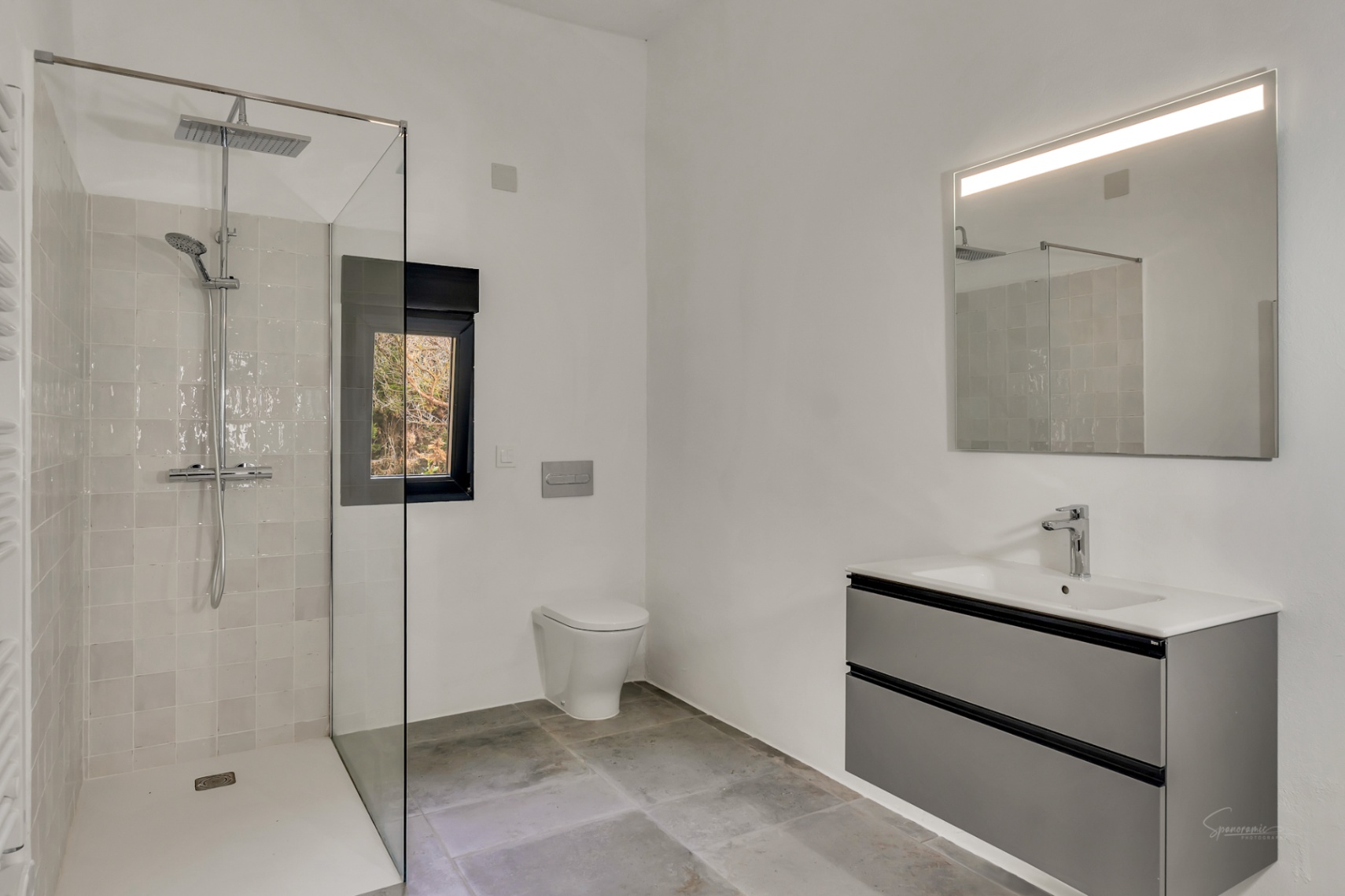Modern bathroom featuring a walk-in shower with glass screen, wall-hung toilet, and a floating grey vanity unit with an illuminated mirror.