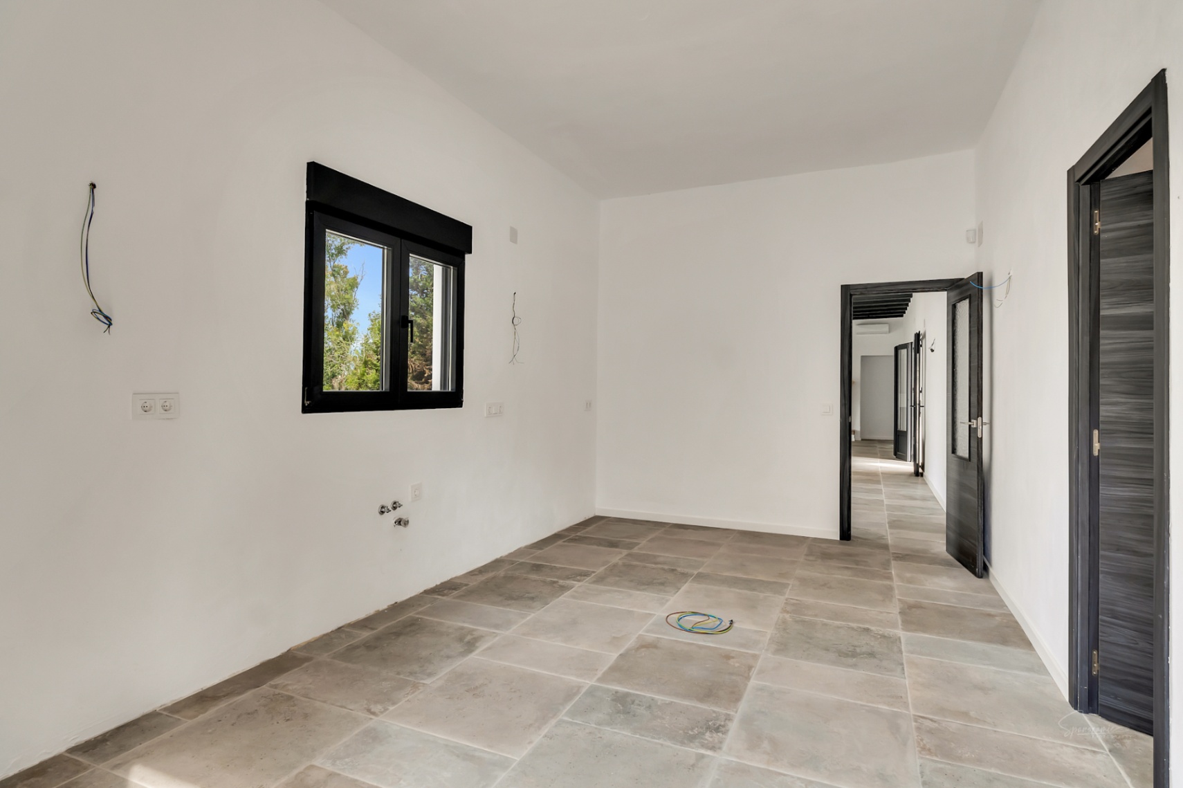Renovated room featuring grey stone-effect floor tiles, white walls, and black window frames. Dark textured doors lead to the bright hallway.