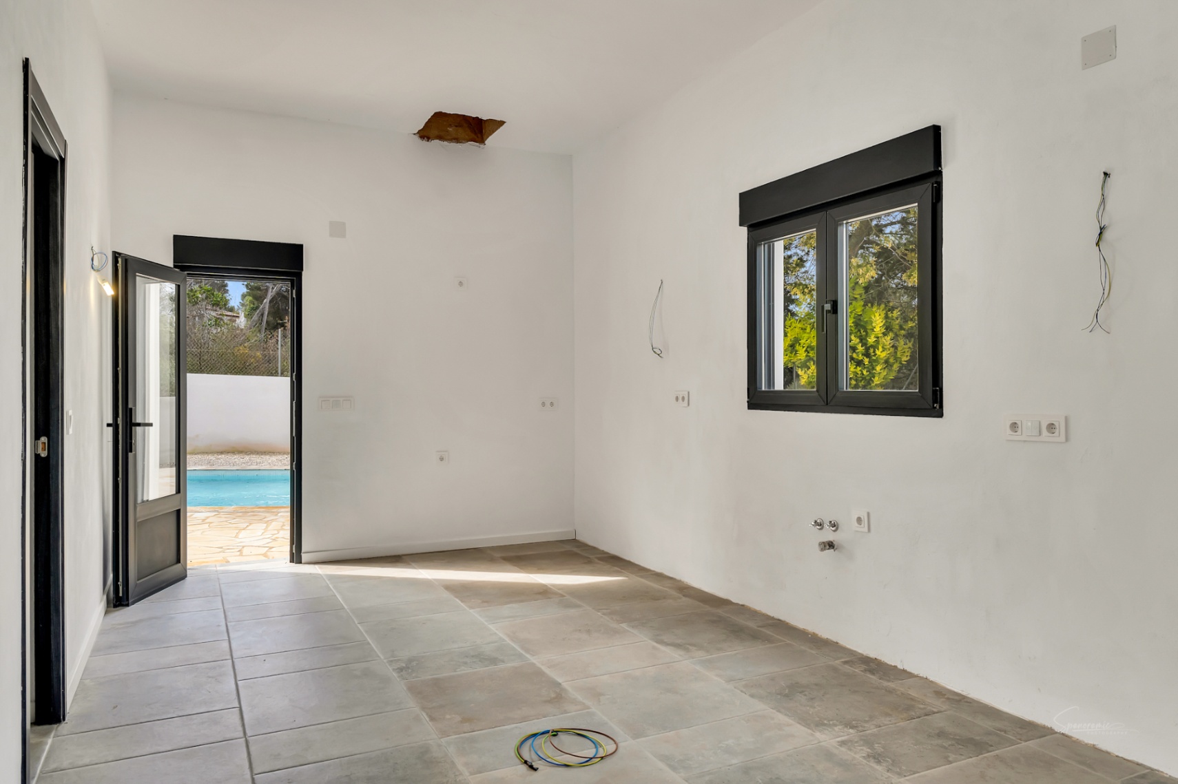 Room under renovation featuring stone-effect floor tiles, black aluminum frames, and direct access to the swimming pool area.