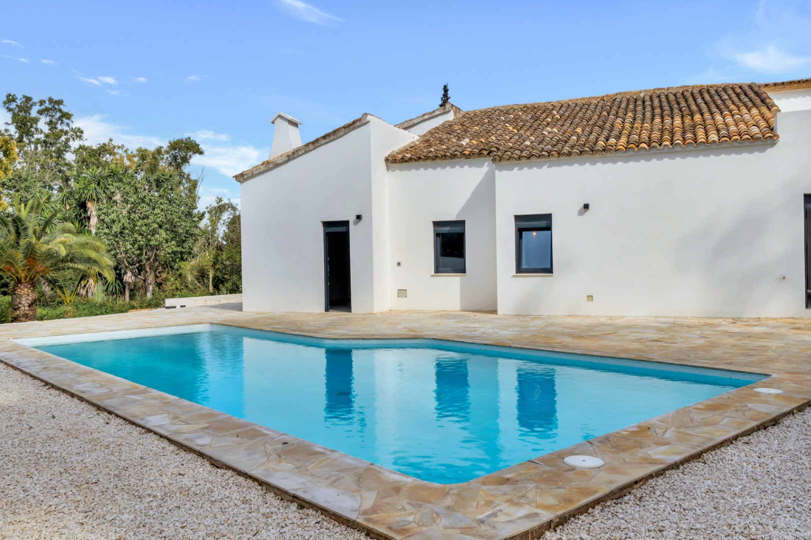 Villa exterior featuring a private swimming pool with a natural stone terrace and white gravel, showcasing Mediterranean architecture with white walls and terracotta tiles.