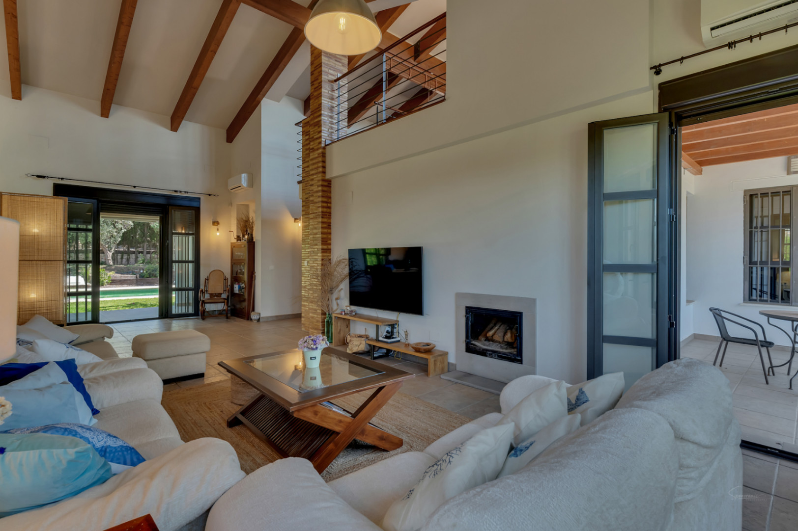 Living room featuring high ceilings with exposed wooden beams, a built-in fireplace, and large glass doors opening to the garden and terrace.