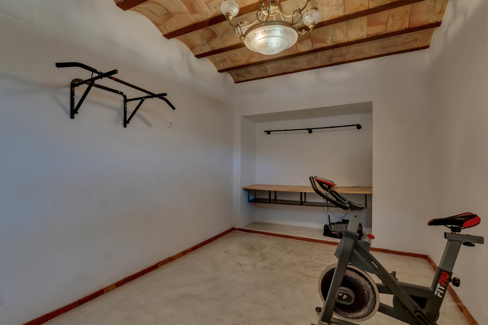 Multipurpose gym area featuring traditional vaulted terracotta ceilings, a wall-mounted pull-up bar, stationary bike, and built-in desk niche.