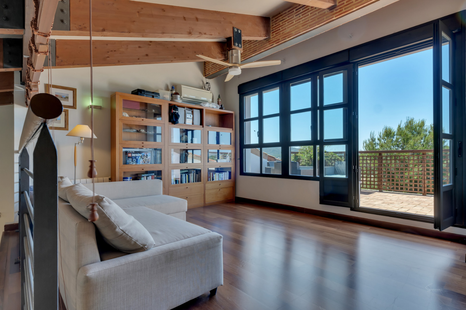 Upper-floor office or bedroom featuring exposed wooden beams, polished wood flooring, and large glass doors opening onto a private sun terrace.