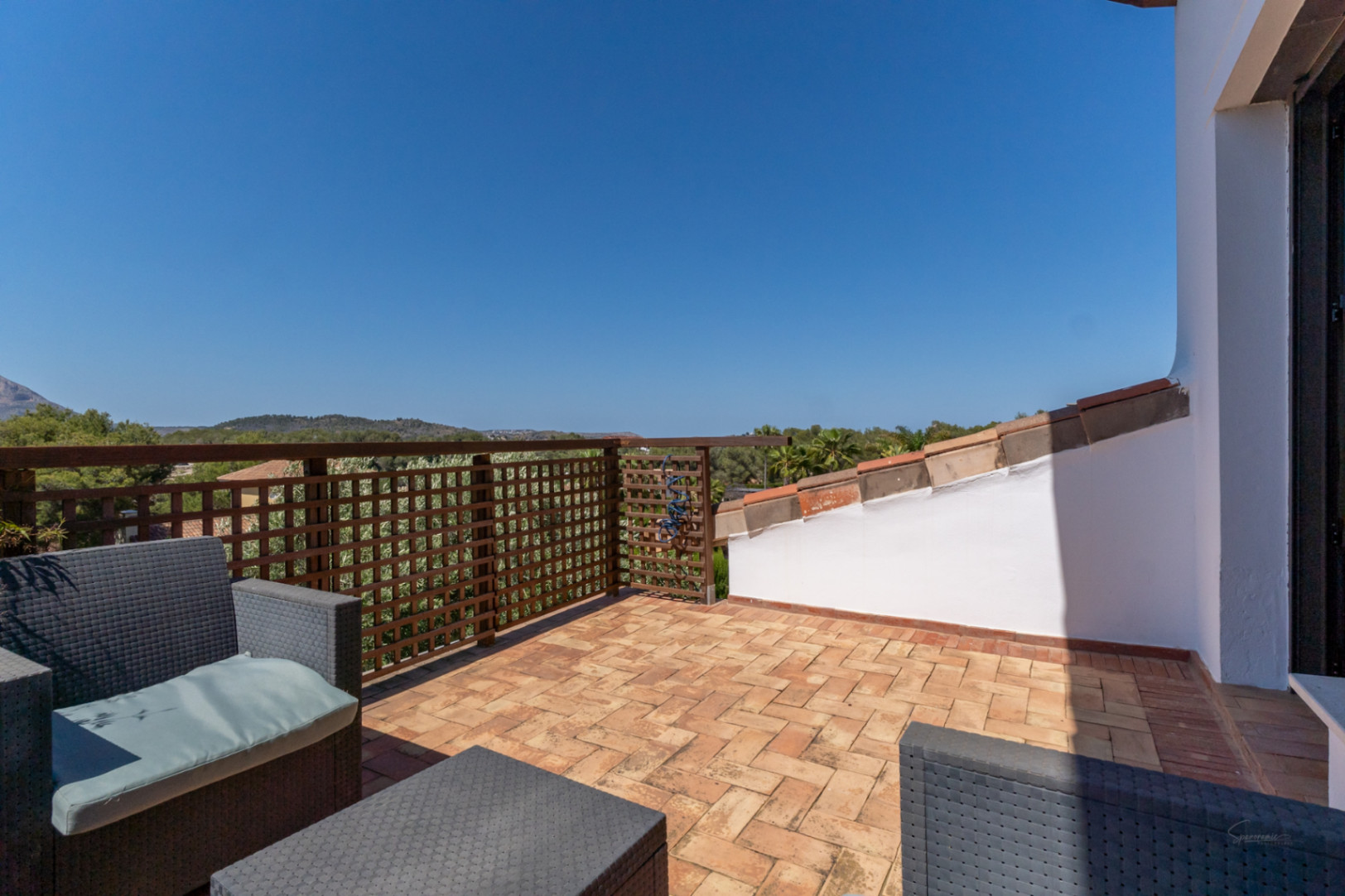 Upper-floor private terrace featuring terracotta tile flooring, grey wicker seating, and a wooden lattice railing overlooking the hills.