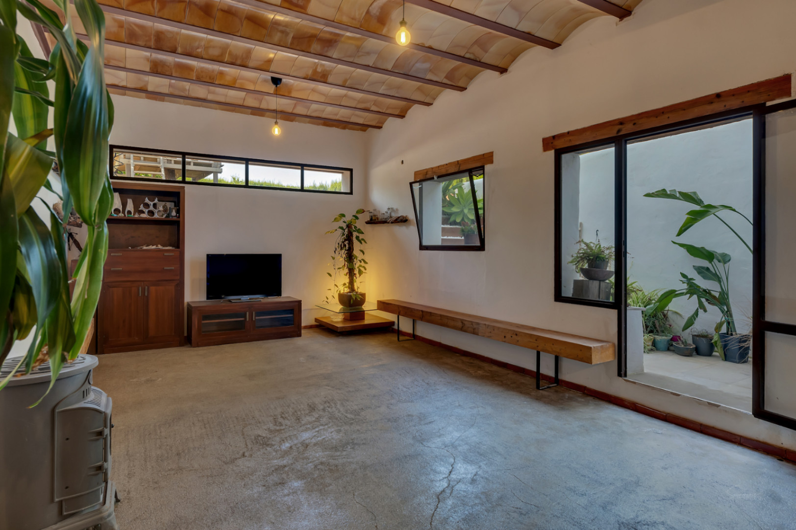 Versatile basement living area featuring traditional vaulted tile ceilings, polished concrete floors, and a glass door opening to a private plant-filled patio.