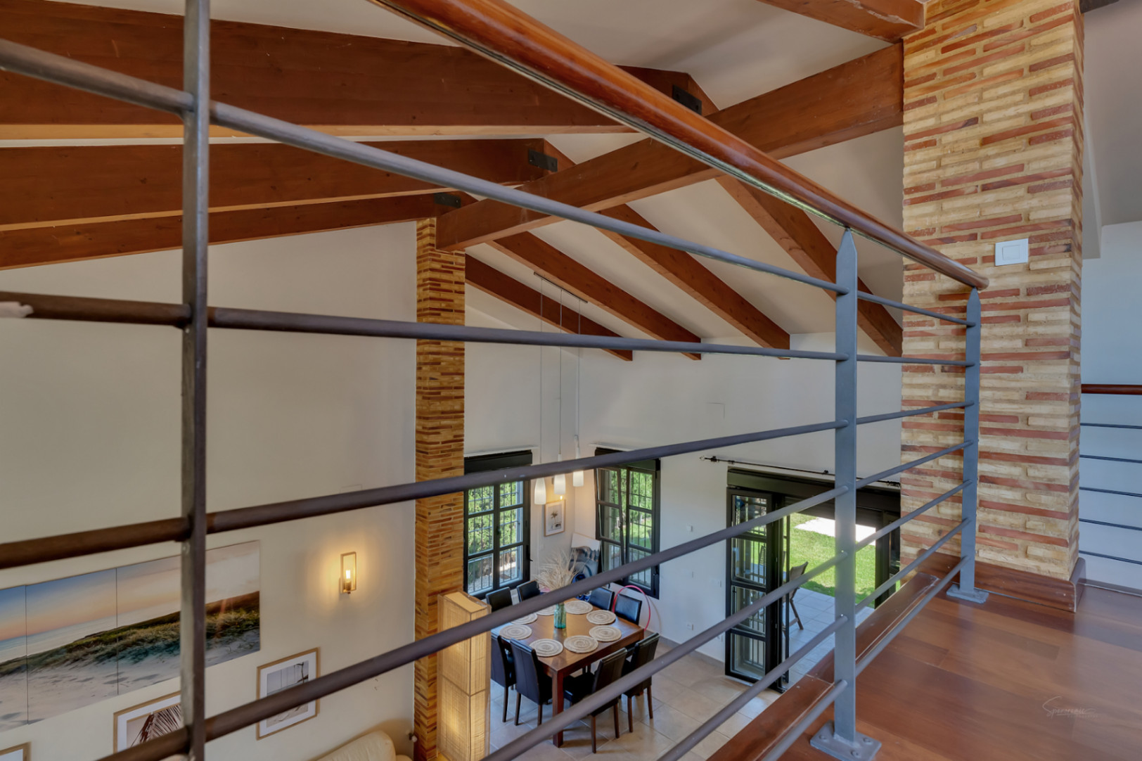 View from the upper floor showcasing high ceilings with exposed wooden beams, decorative brick pillars, and a dining area with garden access.