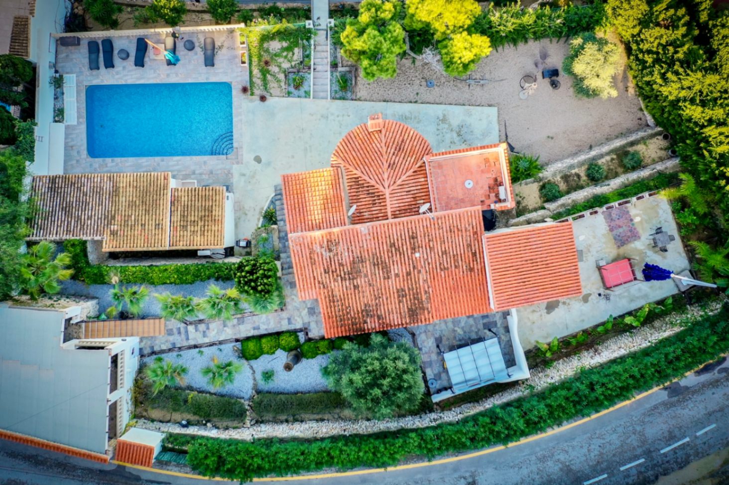 Aerial drone view showing the villa's terracotta roof, the rectangular swimming pool with sun terrace, and the landscaped Mediterranean gardens across the 1,205 m² plot.