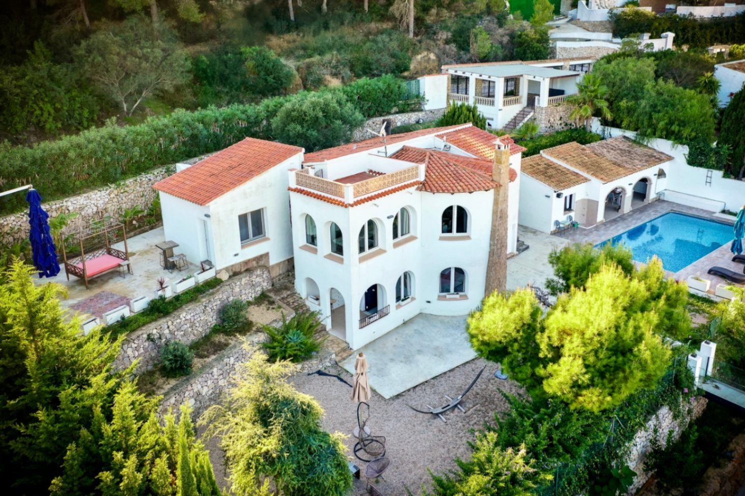 Aerial view of the Mediterranean villa featuring white facades, terracotta roofs, and arched windows. The property includes a private pool, outdoor kitchen, and stone-walled terraces.