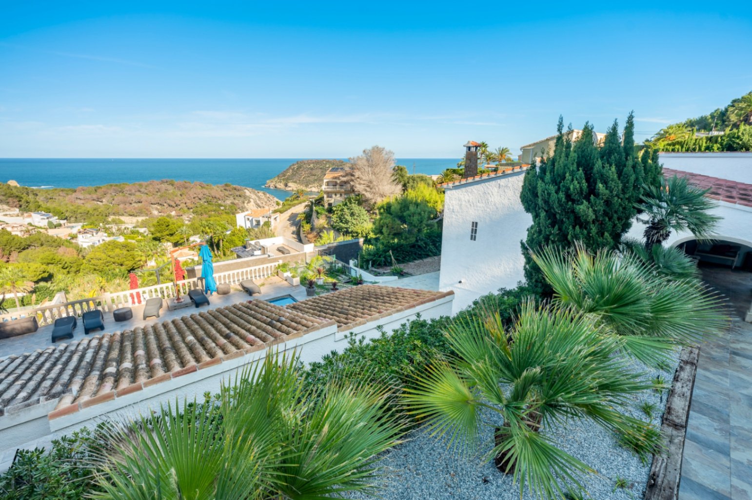 Elevated panoramic view featuring traditional terracotta roof tiles, a sun terrace with loungers, and expansive vistas of the Mediterranean coastline and Portitxol.