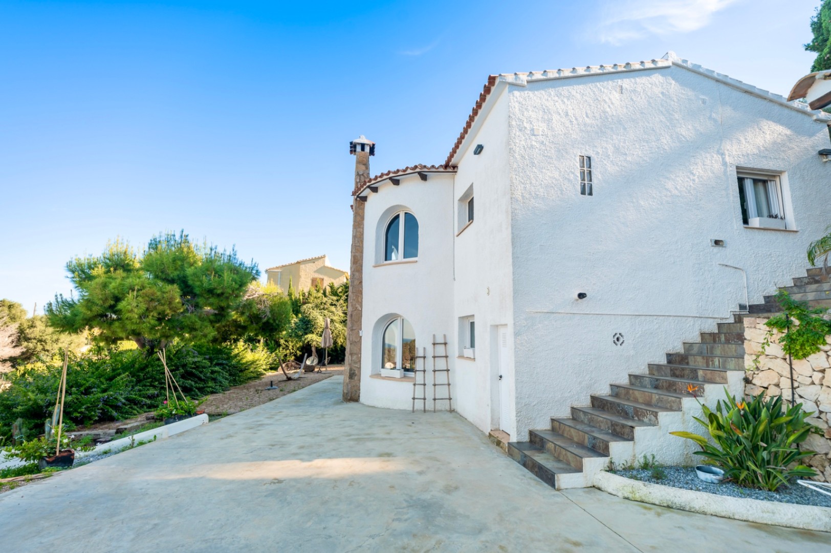 Mediterranean facade featuring white textured walls, arched windows, and a stone chimney, with an external staircase leading to the upper floor.