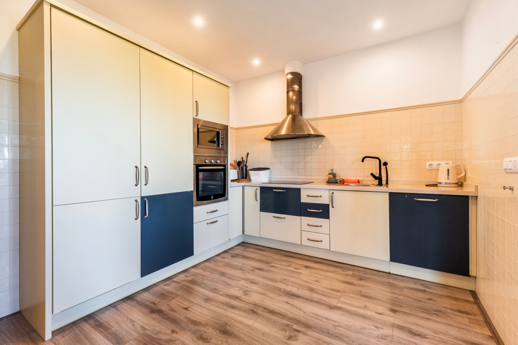 Modern kitchen featuring two-tone cream and blue cabinetry, integrated stainless steel appliances, a sleek black faucet, and wood-effect laminate flooring.