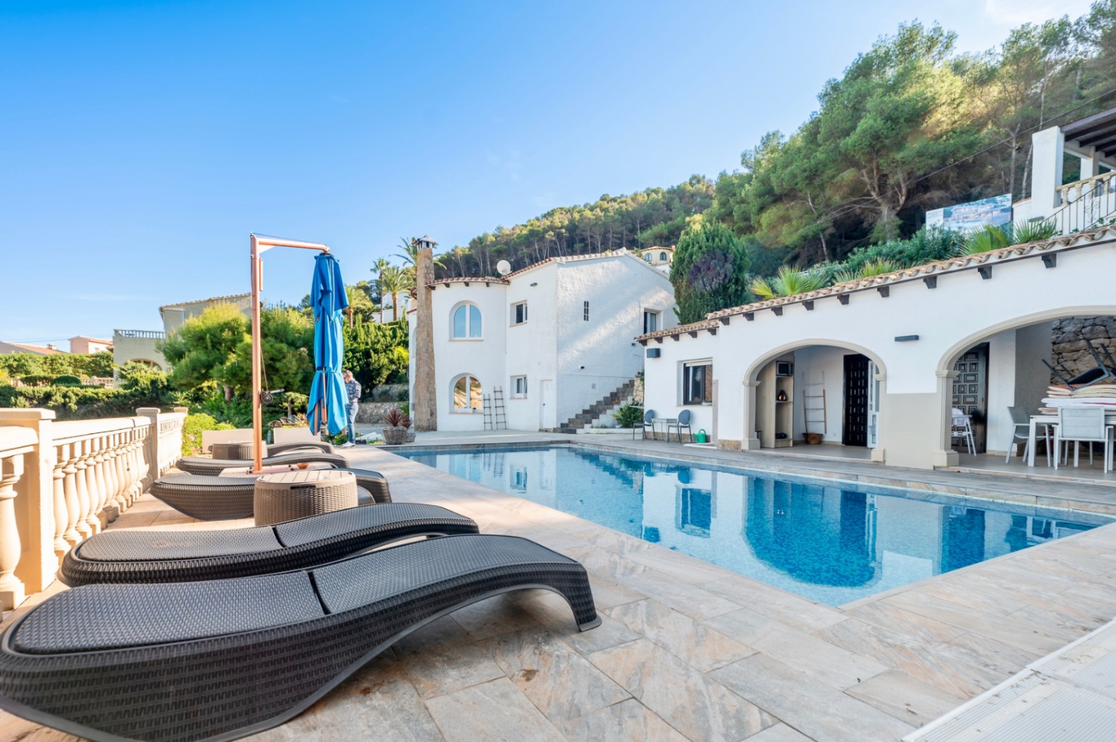 Outdoor terrace featuring a rectangular swimming pool, ergonomic sun loungers, and traditional arched porches set against the villa's white facade.