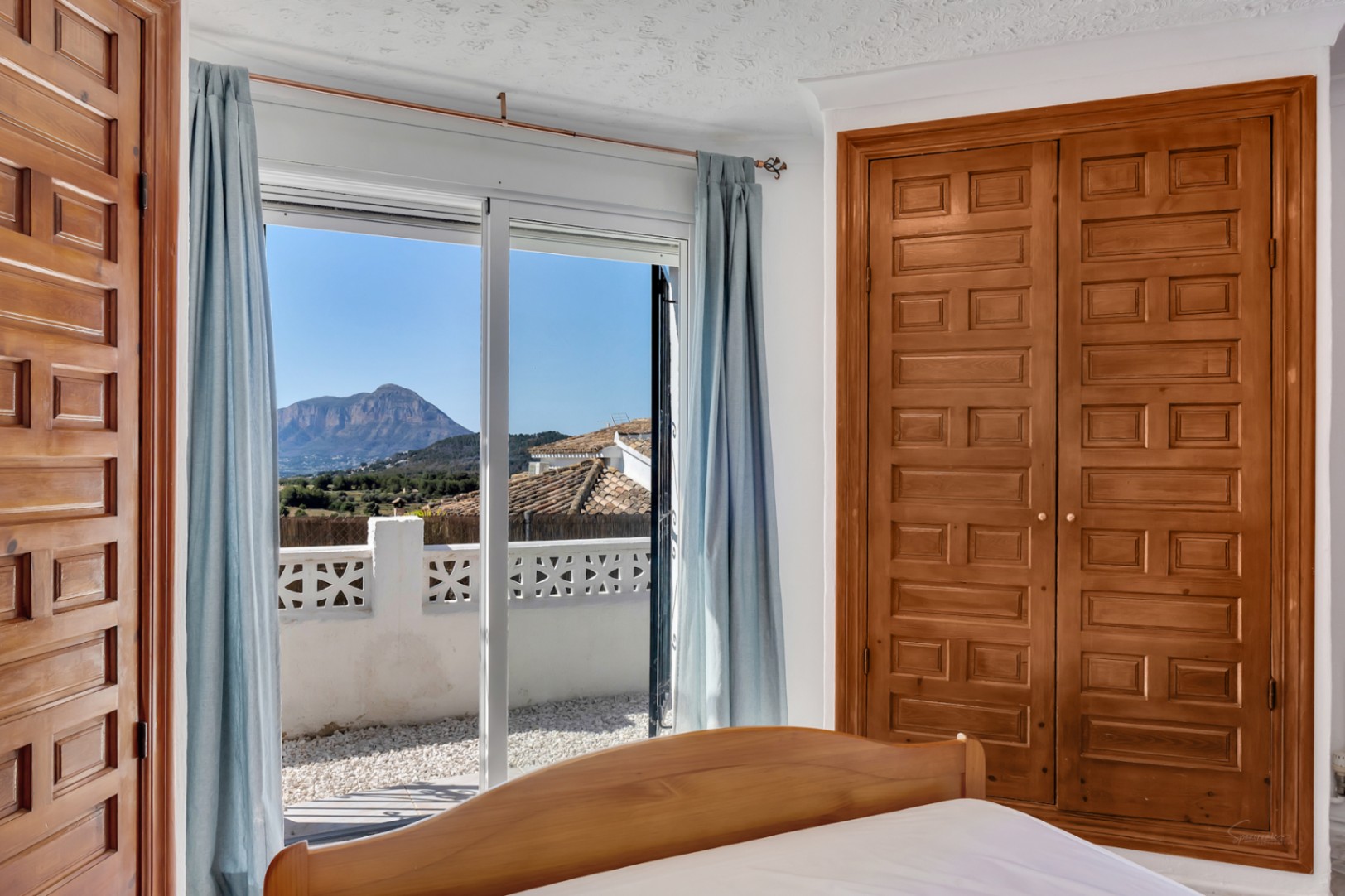 Bedroom featuring a built-in wooden wardrobe and sliding doors opening onto a terrace with panoramic views of the Montgó mountain.