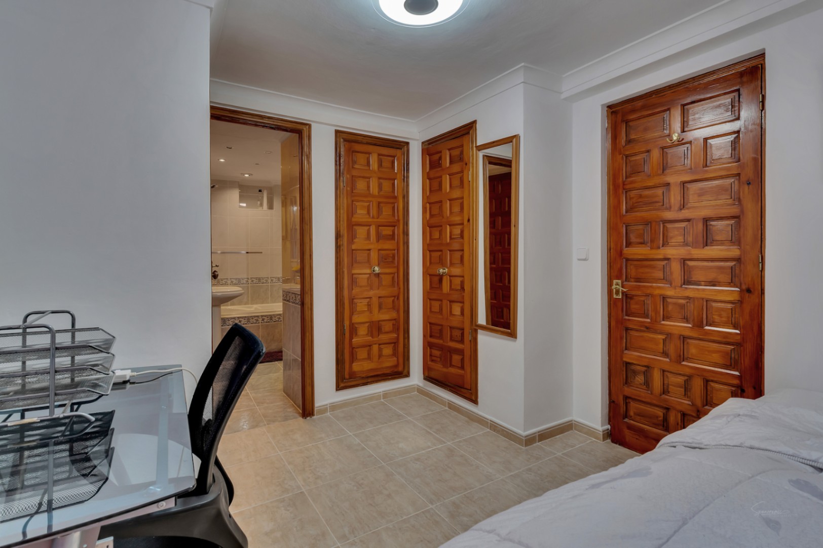 Bedroom featuring built-in solid wood wardrobes, ceramic tile flooring, and direct access to an en-suite bathroom. Includes a practical workspace.
