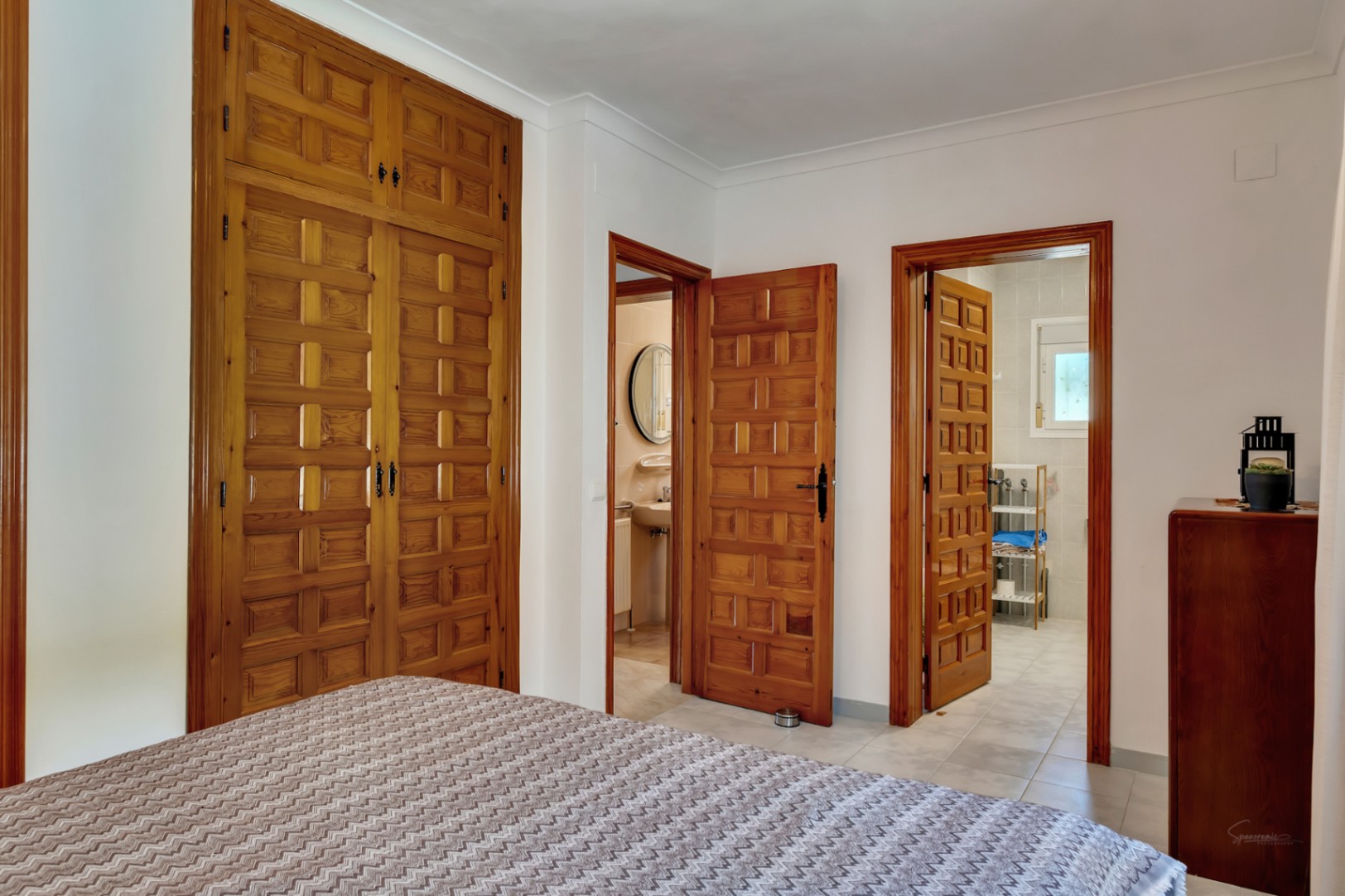 Bedroom featuring large built-in wooden wardrobes with traditional paneling and two doorways leading to en-suite bathrooms with tiled finishes.
