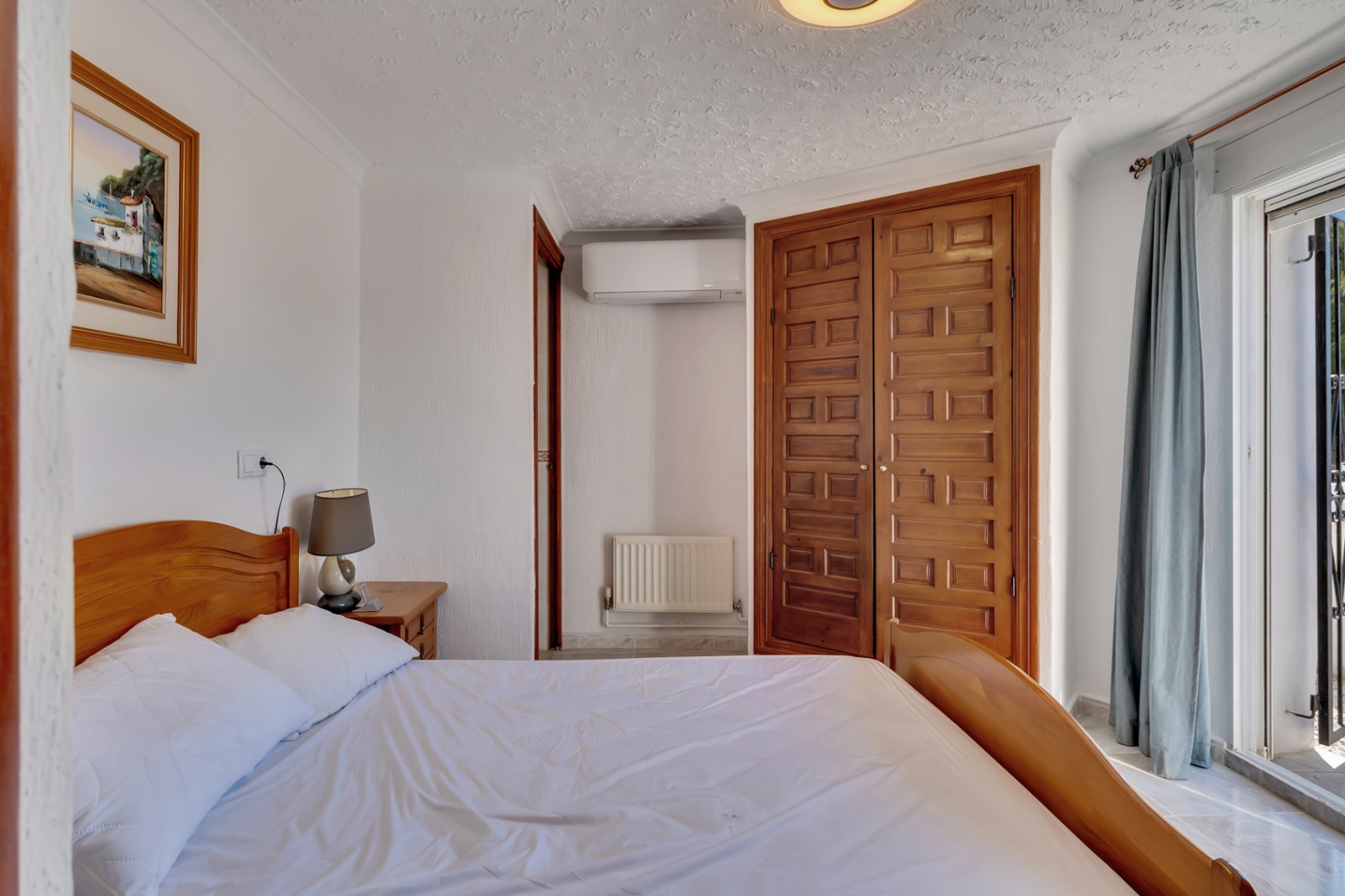 Bright bedroom featuring a wooden bed frame, built-in panelled wardrobes, split air conditioning, and direct access to the terrace through sliding glass doors.