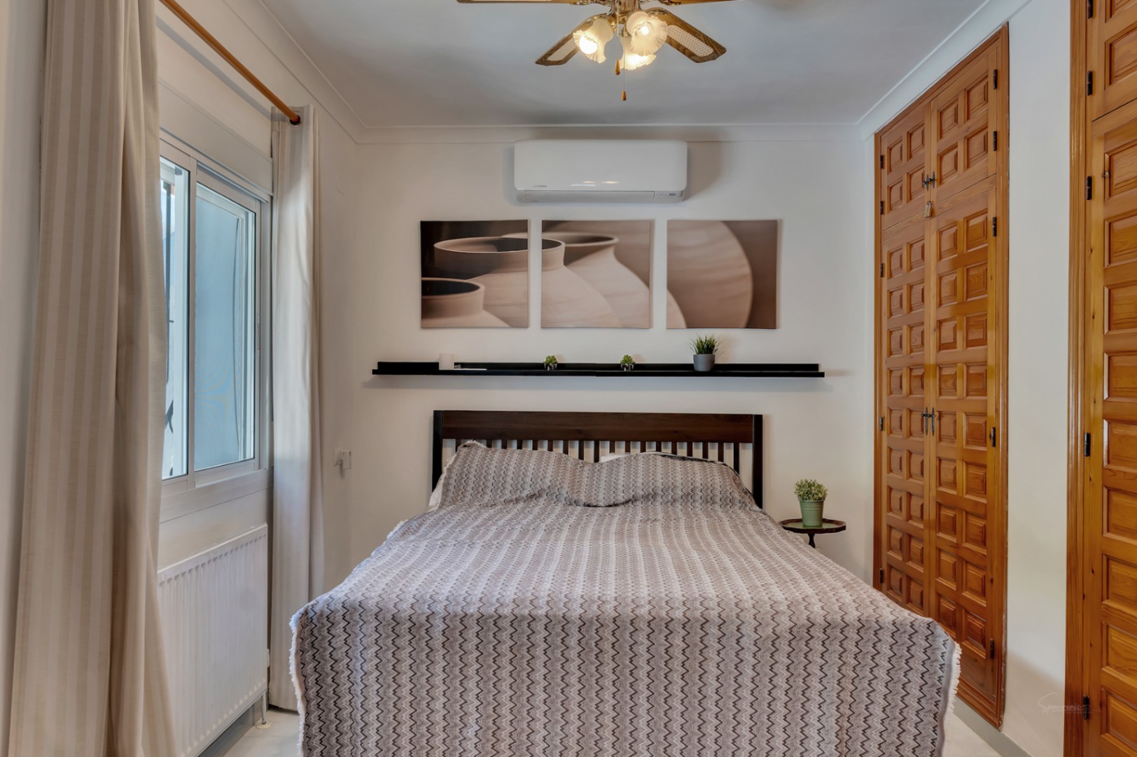 Bright bedroom featuring traditional carved wood built-in wardrobes, air conditioning, a ceiling fan, and double-glazed windows with a radiator.